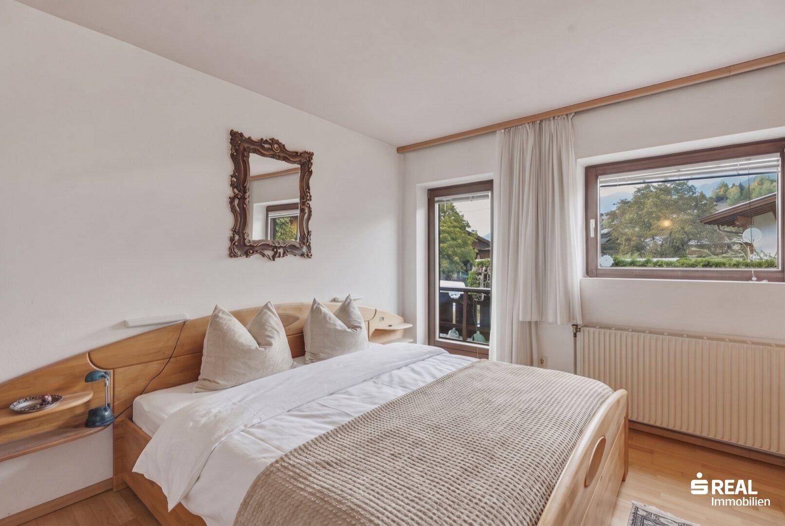 Gemütliches Schlafzimmer mit Holzbett, Balkonzugang und Blick ins Grüne.