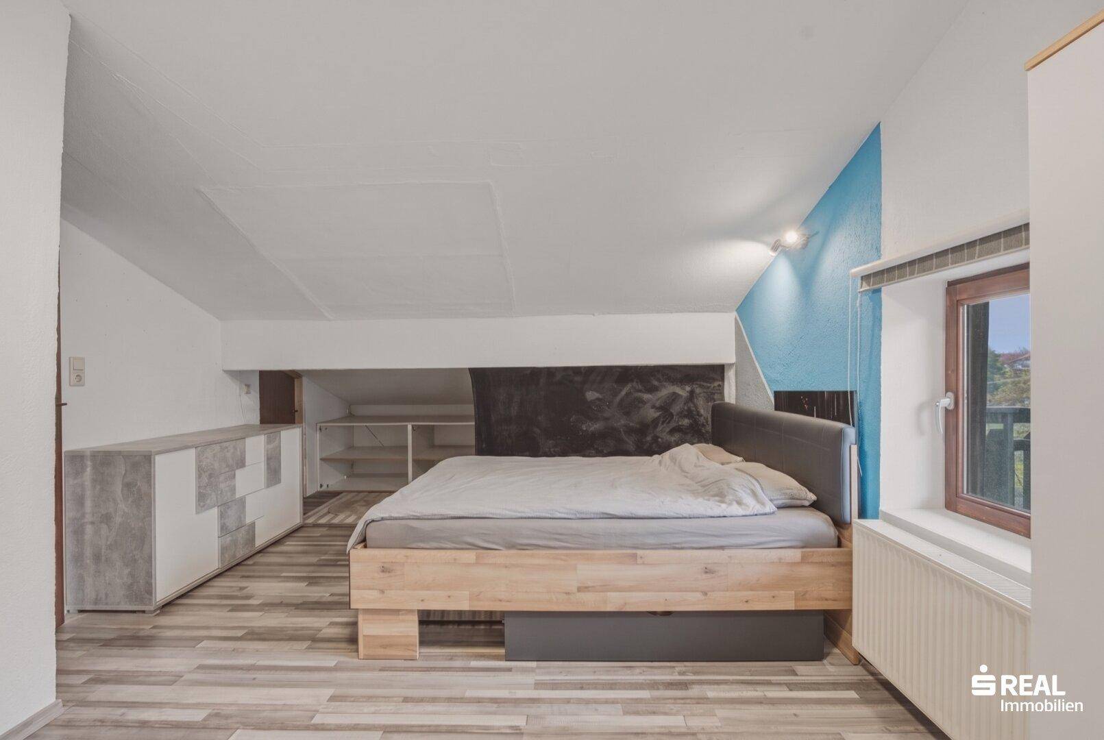 Schlafzimmer mit Holzbett, Stauraum und farbiger Akzentwand im Dachgeschoss.