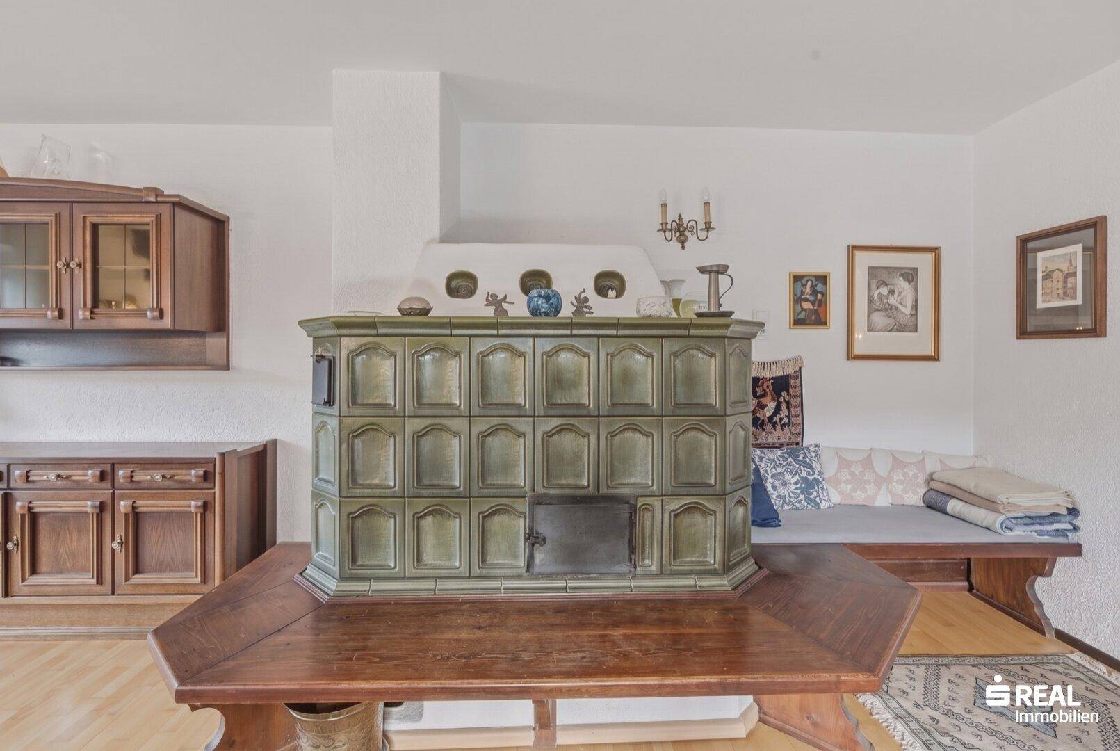 Wohnzimmer mit traditionellem Kachelofen, Holztisch und Sitzbank.