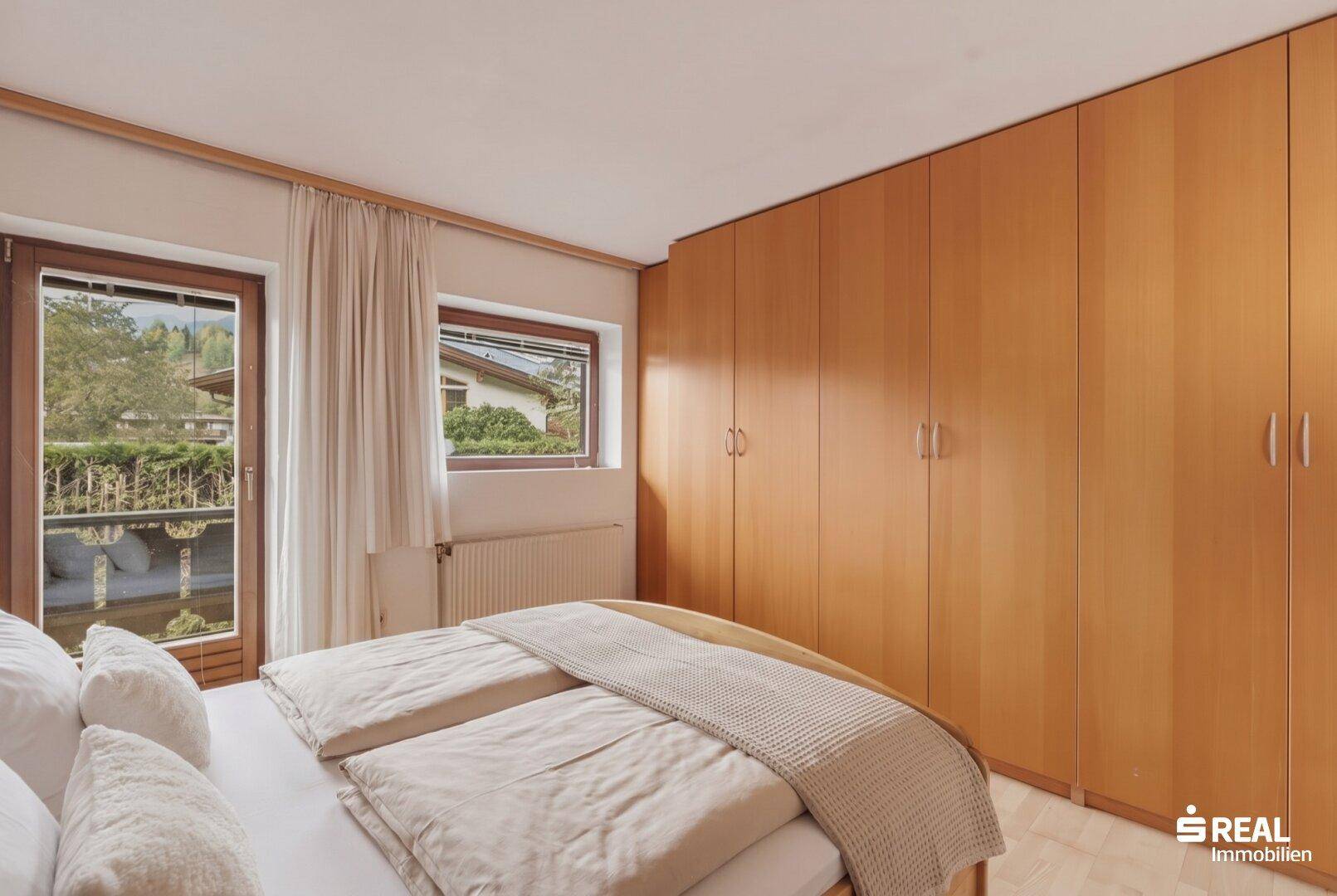 Schlafzimmer mit hellem Holzschrank, Doppelbett und Zugang zum Balkon.