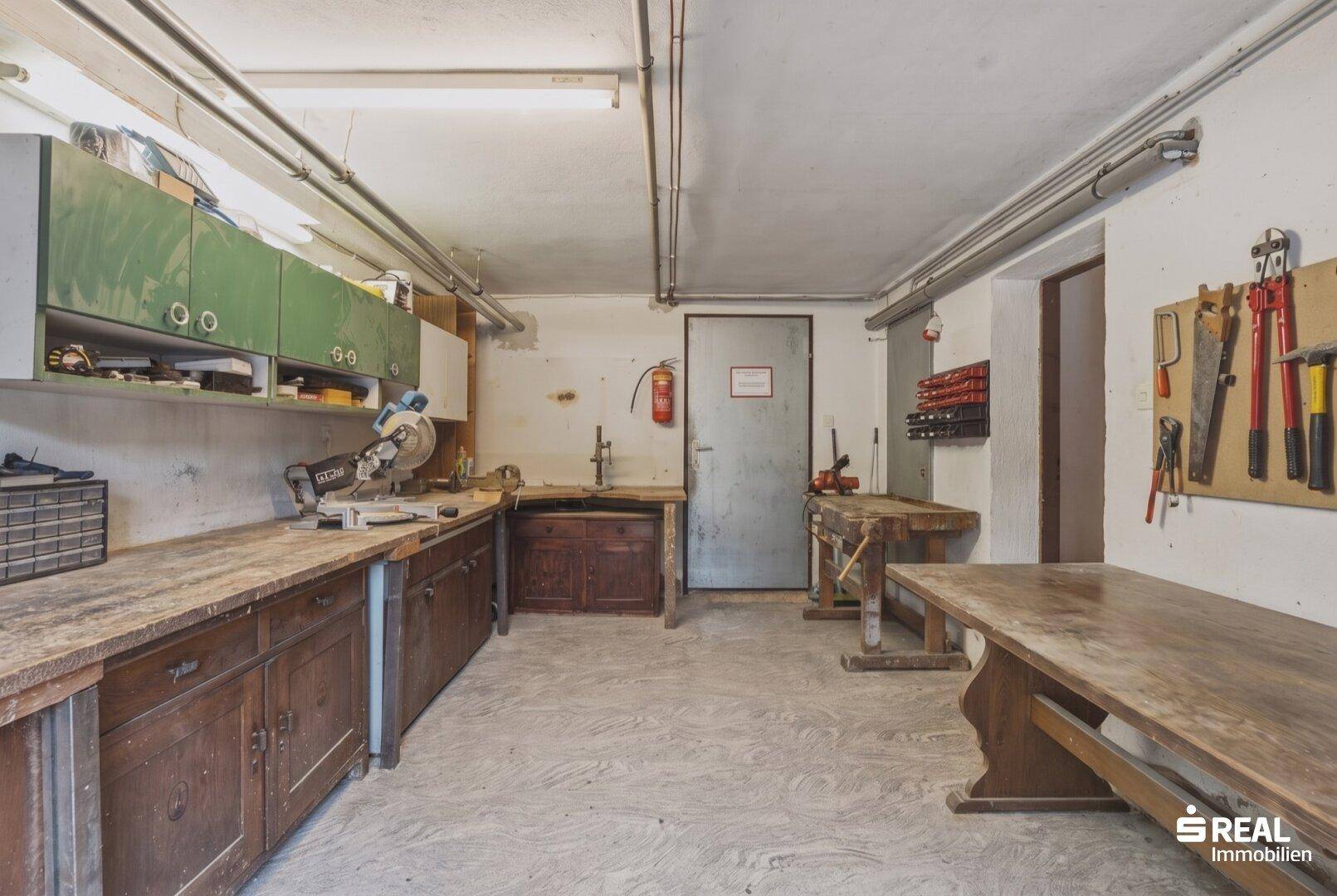 Geräumige Werkstatt im Keller mit Arbeitsbänken und Werkzeugaufbewahrung.