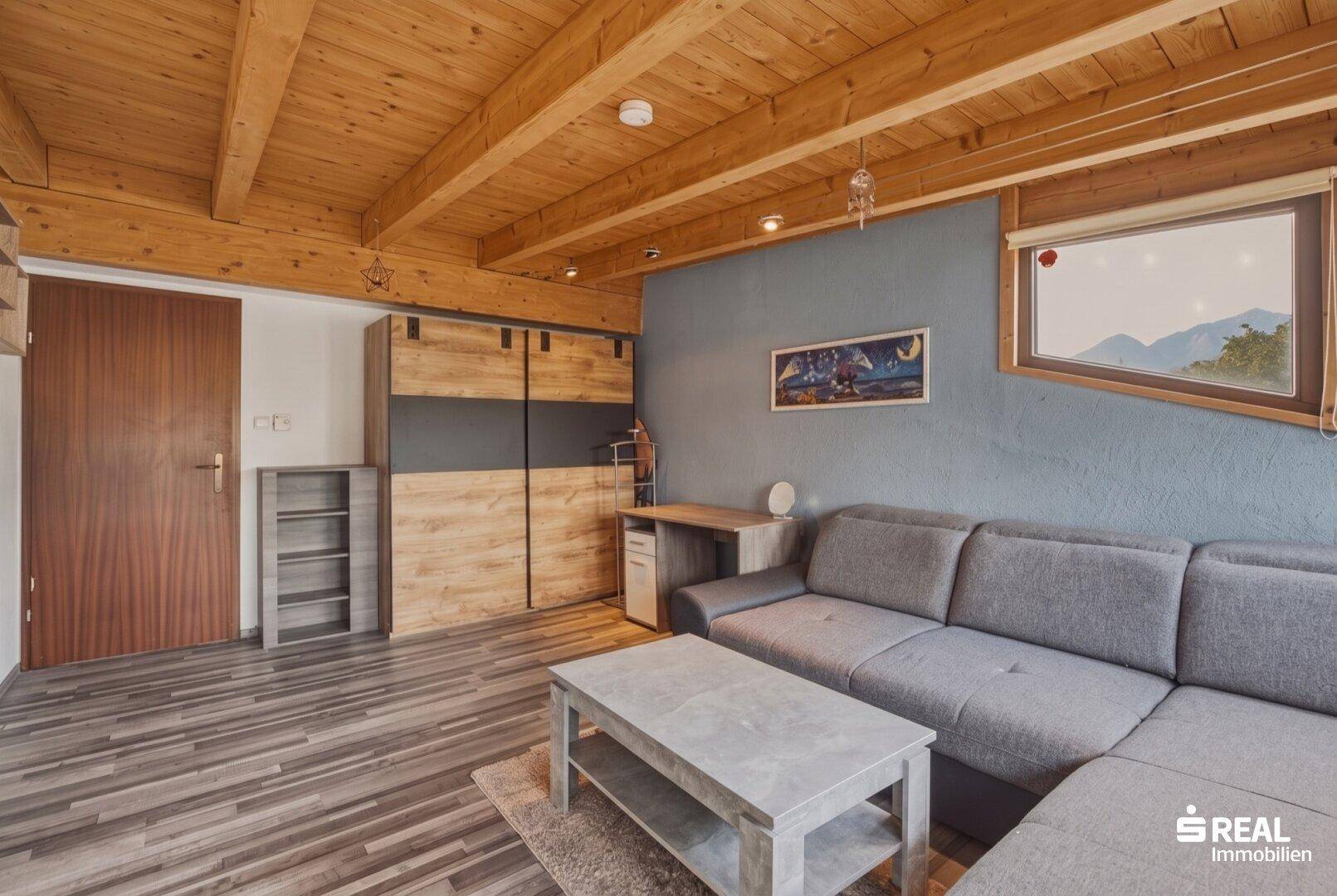 Wohnzimmer mit Holzbalkendecke, modernem Sofa und integrierten Schränken.