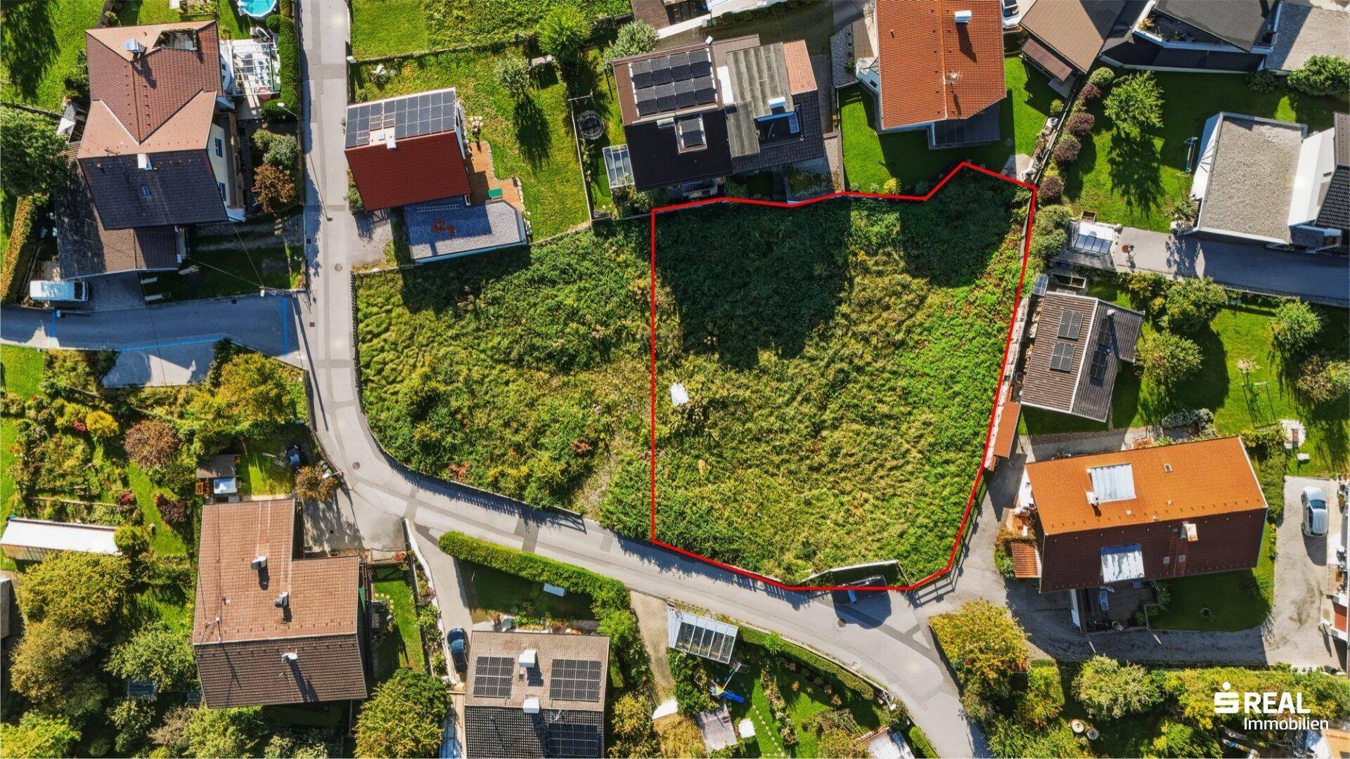 Luftaufnahme eines unbebauten Grundstücks mit roter Umrandung, umgeben von Wohnhäusern und Straßen.