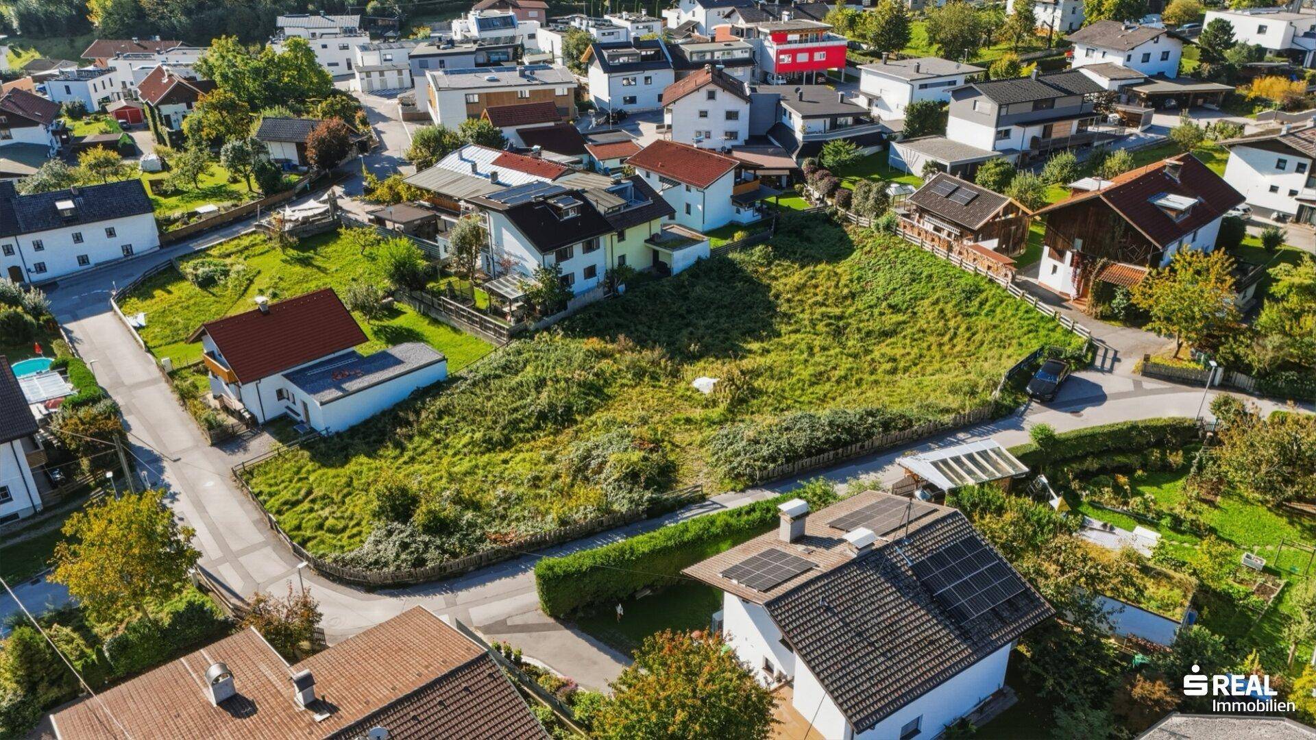 Luftaufnahme eines unbebauten Grundstücks in einer sonnigen Wohngegend mit Blick auf die umliegenden Häuser.