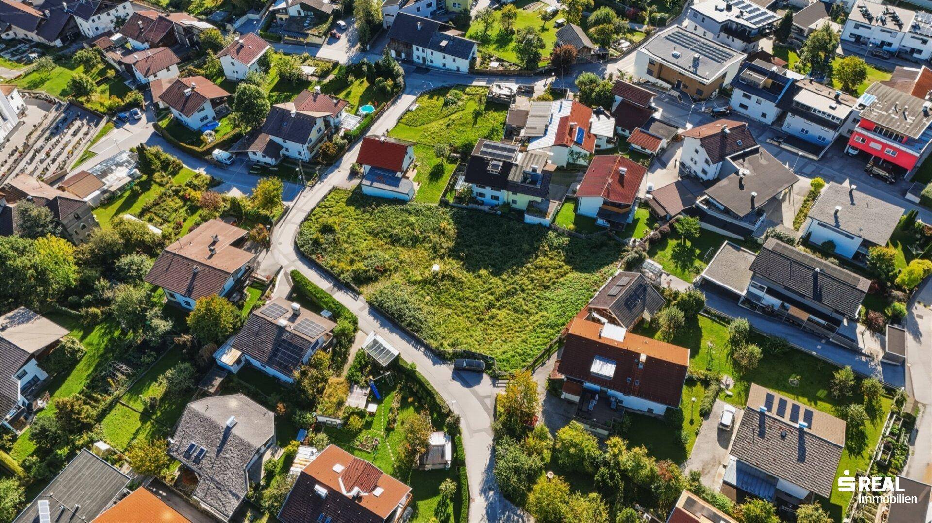 Weitläufige Luftaufnahme eines unbebauten Grundstücks und der umliegenden Wohnsiedlung mit viel Grün.