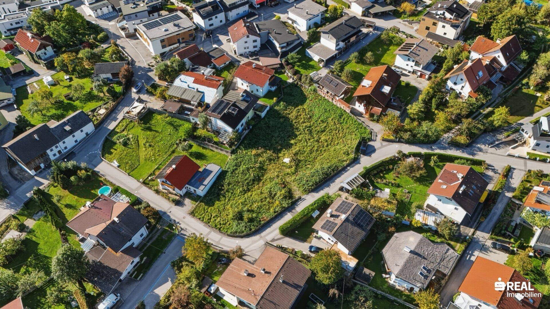 Übersichtliche Luftaufnahme eines unbebauten Grundstücks, eingebettet in eine Wohnsiedlung mit vielen Gärten.