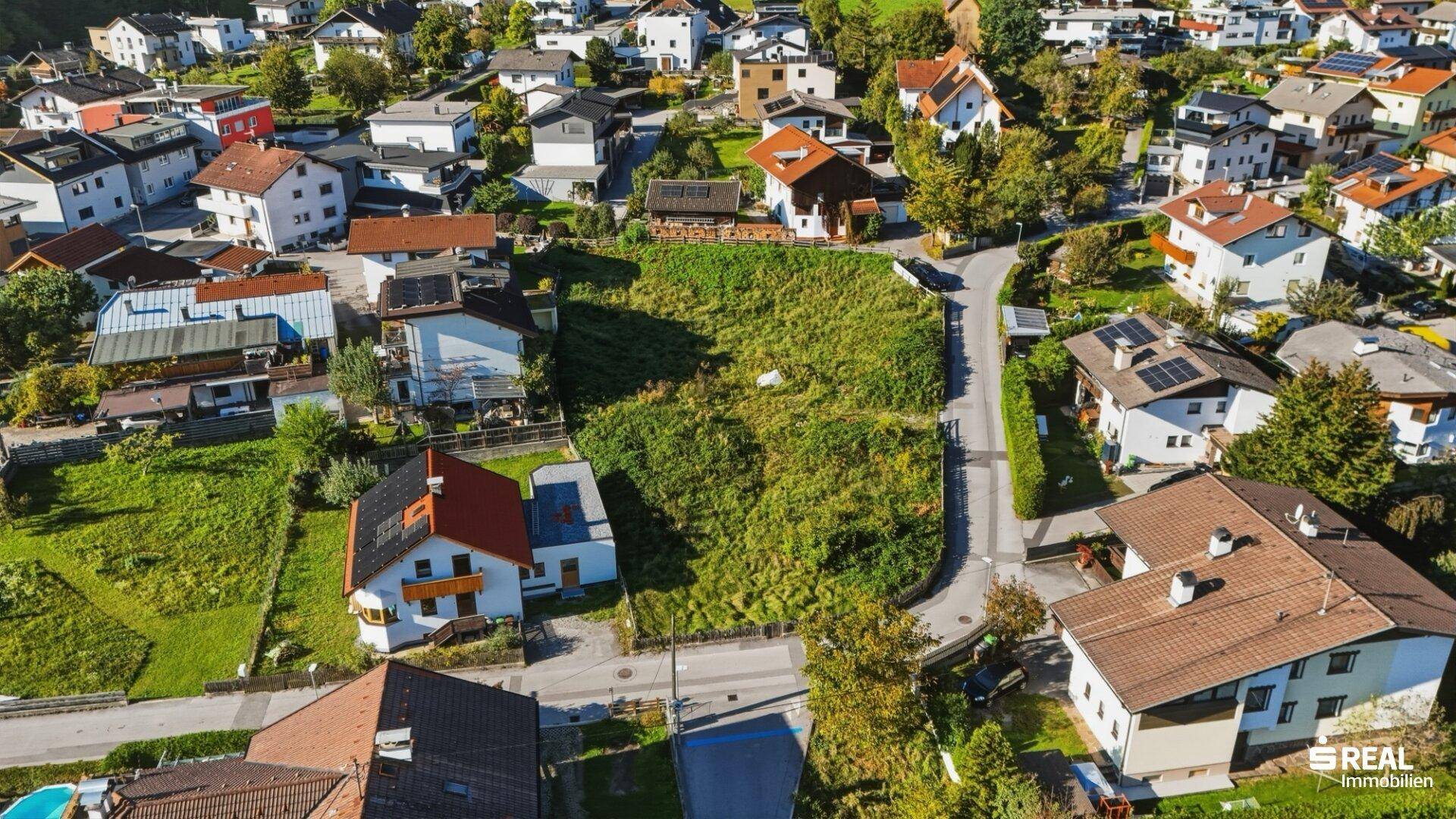 Detaillierte Luftaufnahme eines unbebauten Grundstücks mit angrenzenden Wohnhäusern und Straßenverlauf.