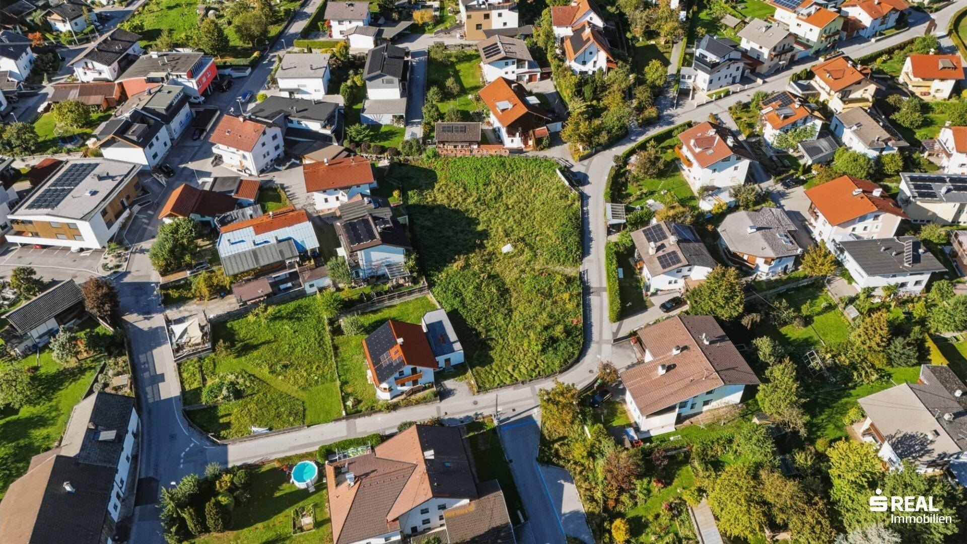 Luftaufnahme eines großen unbebauten Grundstücks, umgeben von Einfamilienhäusern und grünen Flächen.