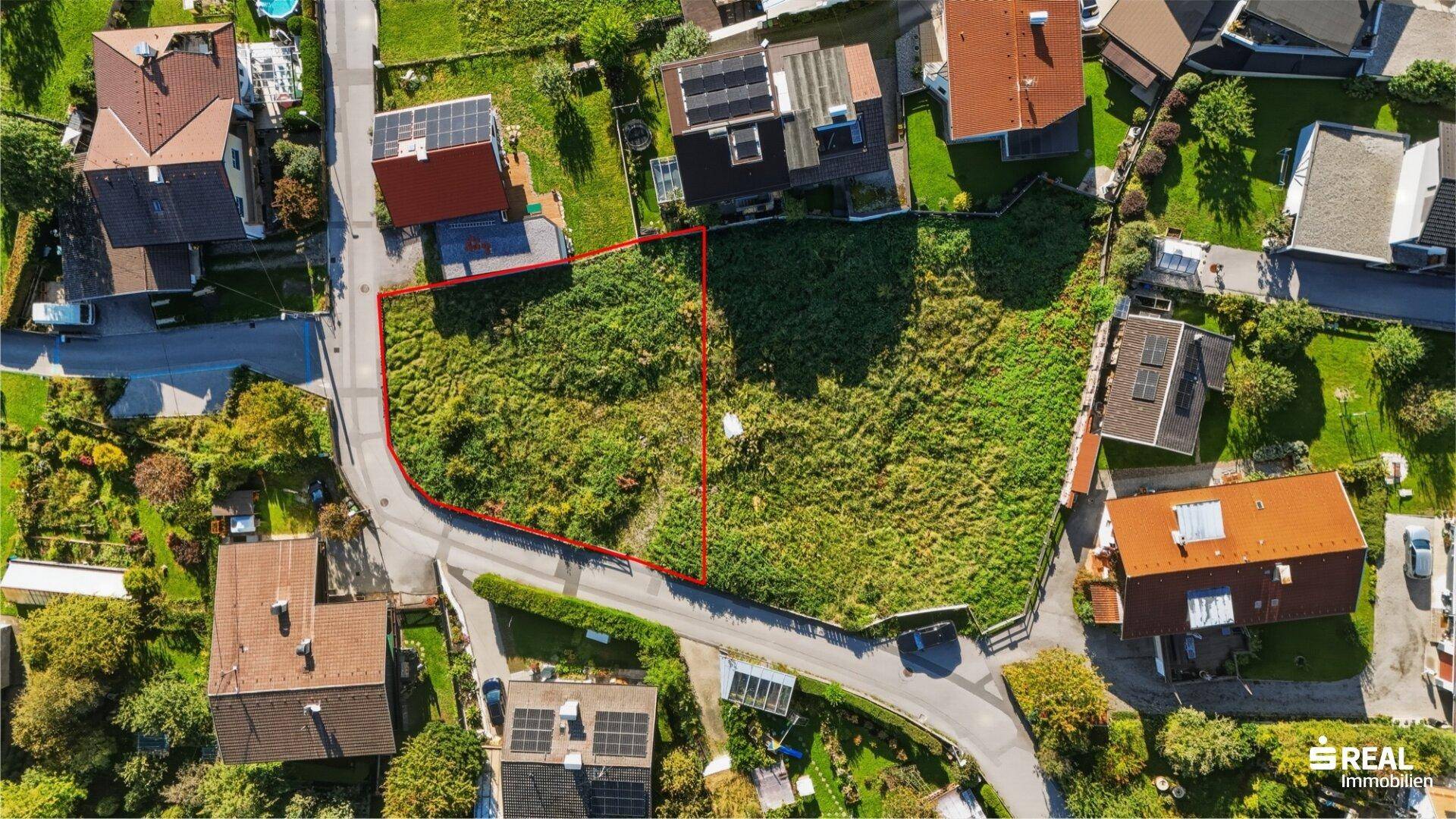 Luftaufnahme eines unbebauten Grundstücks mit roter Markierung, umgeben von Wohnhäusern und Straßen.