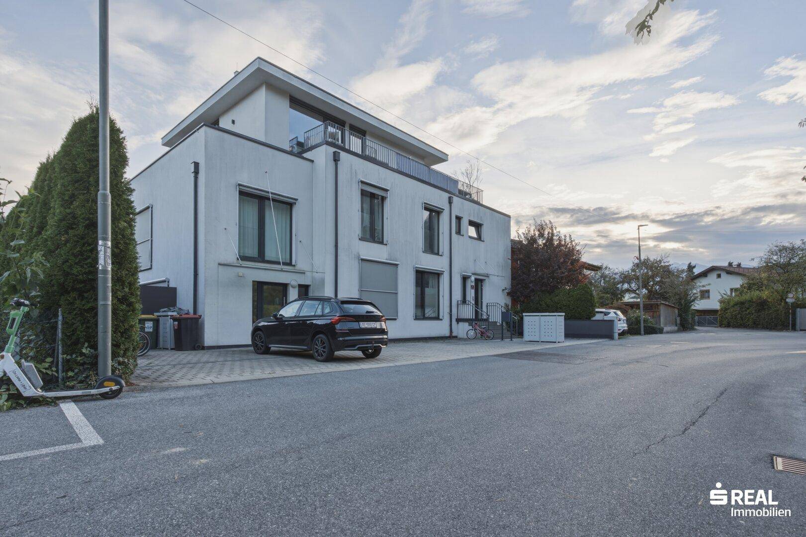 Modernes Mehrfamilienhaus mit weißer Fassade, großen Fenstern und Parkplätzen.