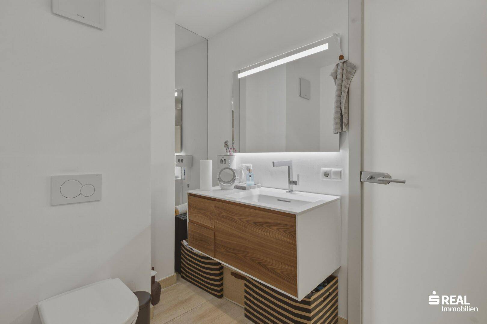 Modernes Badezimmer mit Waschtisch, beleuchtetem Spiegel und Wand-WC.