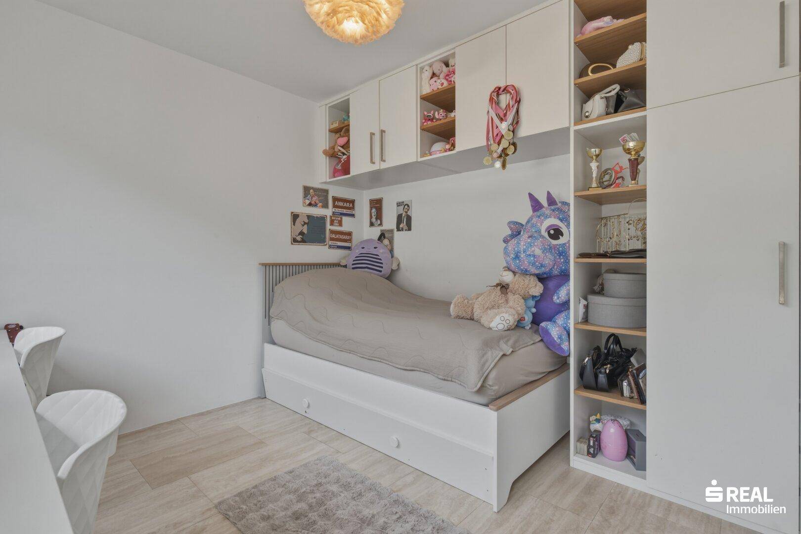 Kinderzimmer mit Einzelbett, integrierten Schränken und Regalen für Spielzeug und Bücher.