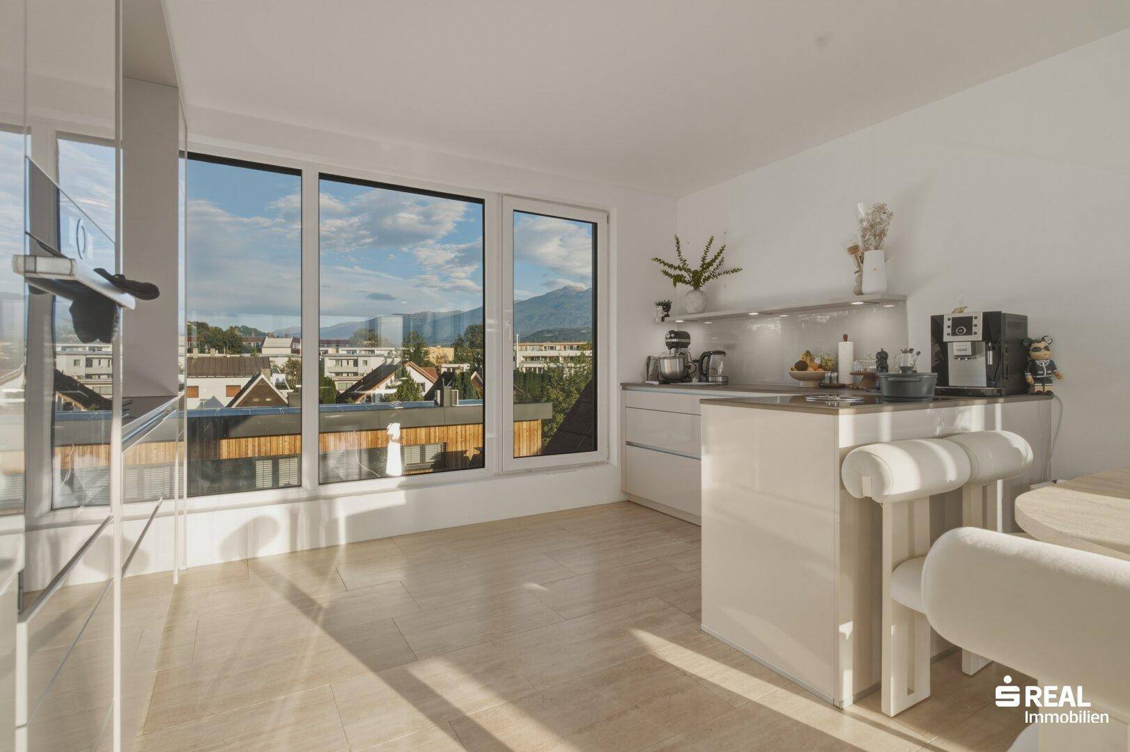 Moderne Küche mit hellen Fronten, Arbeitsfläche und großem Fenster mit Bergblick.