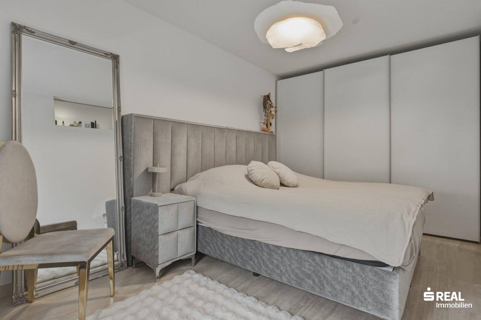 Gemütliches Schlafzimmer mit großem Bett, Kleiderschrank und modernem Spiegel.