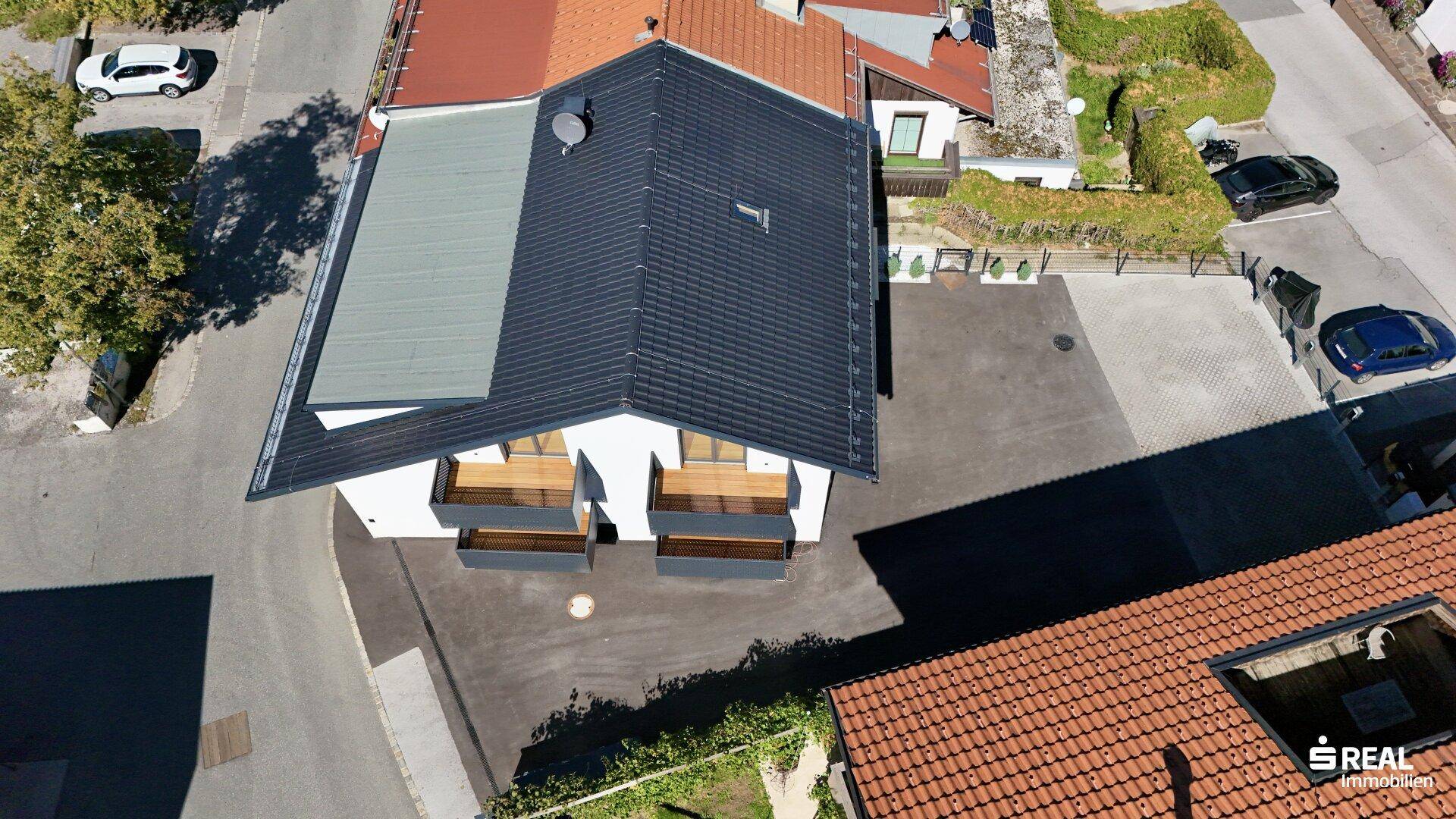 Draufsicht auf ein modernes Gebäude mit dunklem Dach, Balkonen und Parkplätzen im Freien.