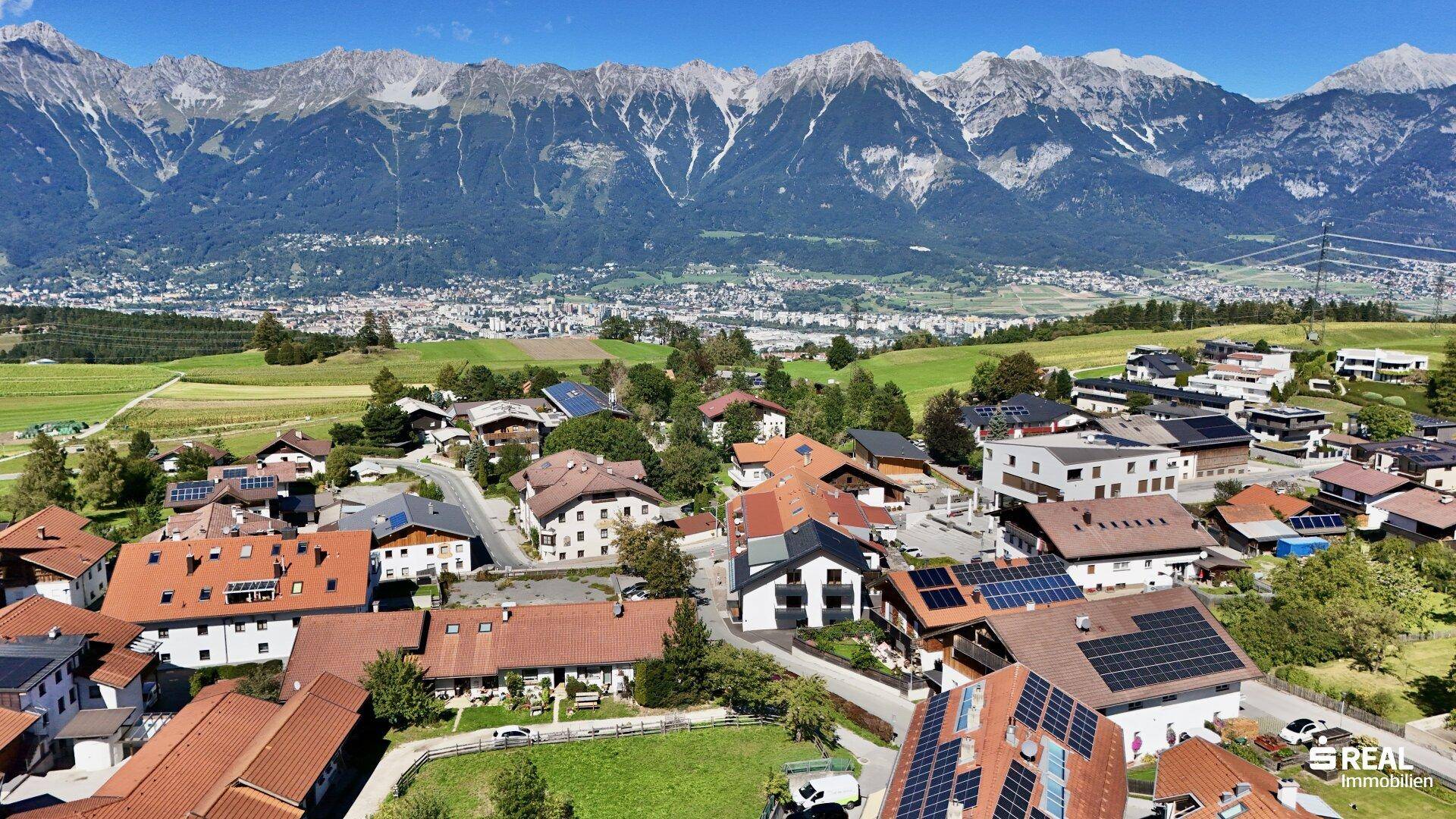 Weitläufige Luftaufnahme eines Dorfes mit Blick auf eine Stadt und imposante schneebedeckte Berge.
