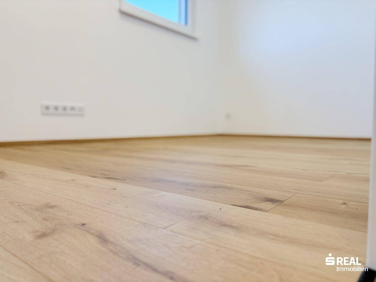 Nahaufnahme eines hellen Holzbodens und einer weißen Wand mit einer Steckdose.