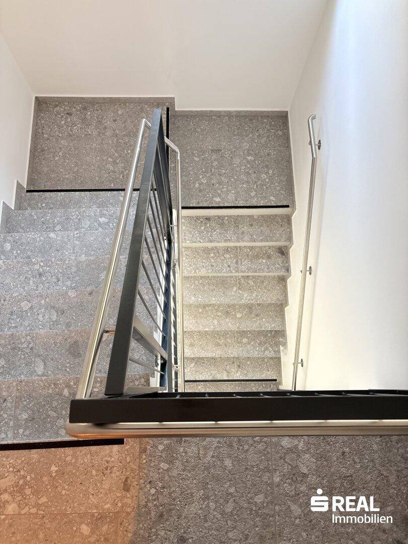 Modernes Treppenhaus mit grauen Fliesen und einem eleganten Metallgeländer, das die Stockwerke verbindet.