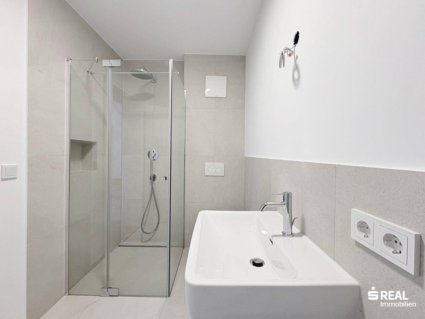 Helles, modernes Badezimmer mit Glasdusche, Waschbecken und wandhängendem WC in neutralen Farbtönen.