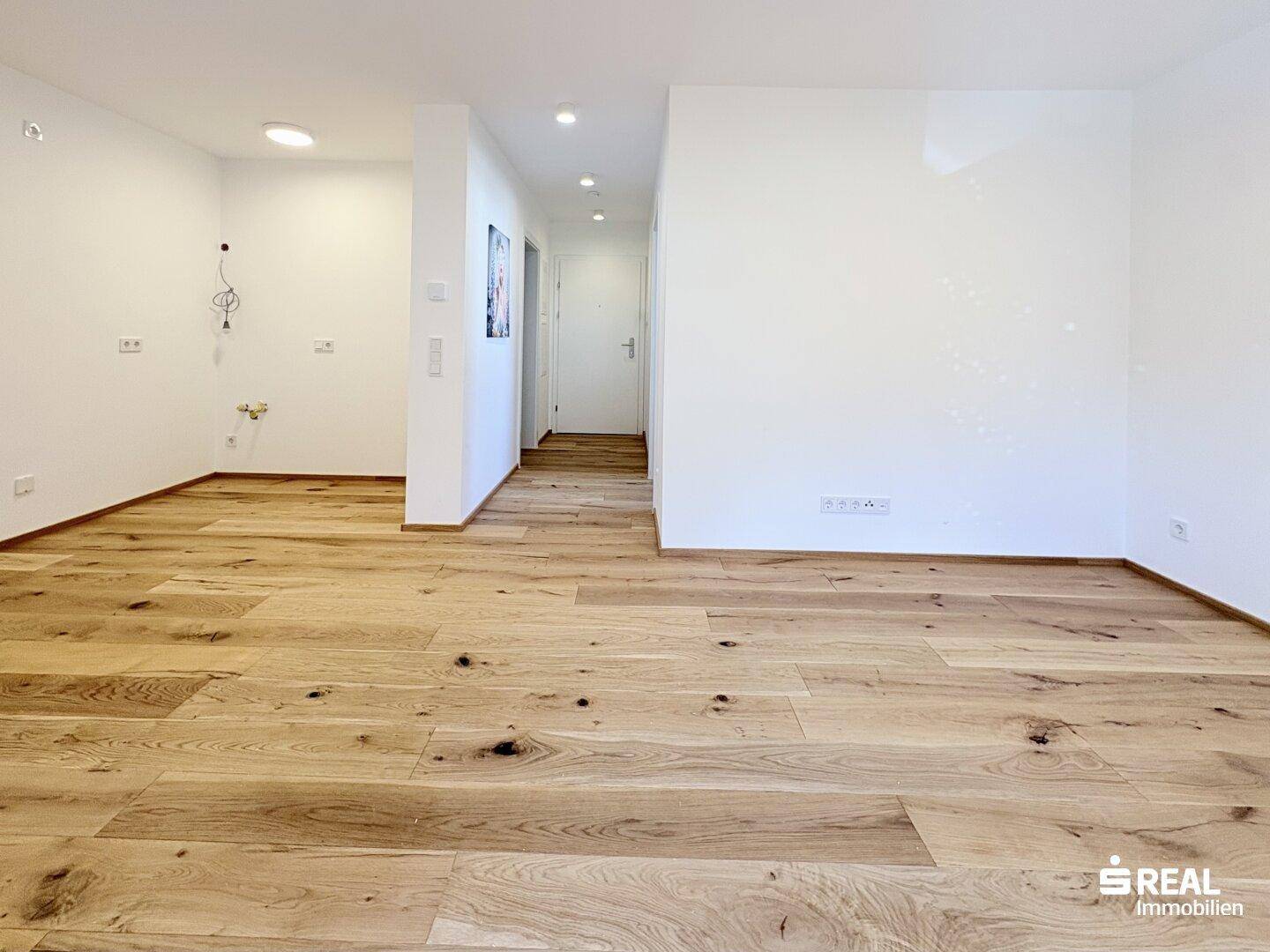 Langer, heller Flur mit Holzboden, weißen Wänden und integrierter Deckenbeleuchtung.