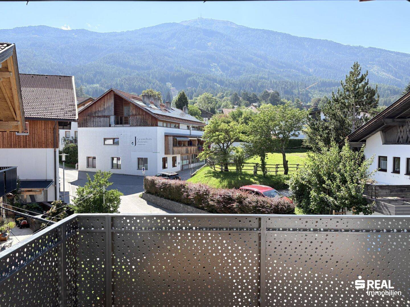 Balkon mit perforiertem Geländer und weitem Blick auf die umliegende Berglandschaft und Nachbargebäude.