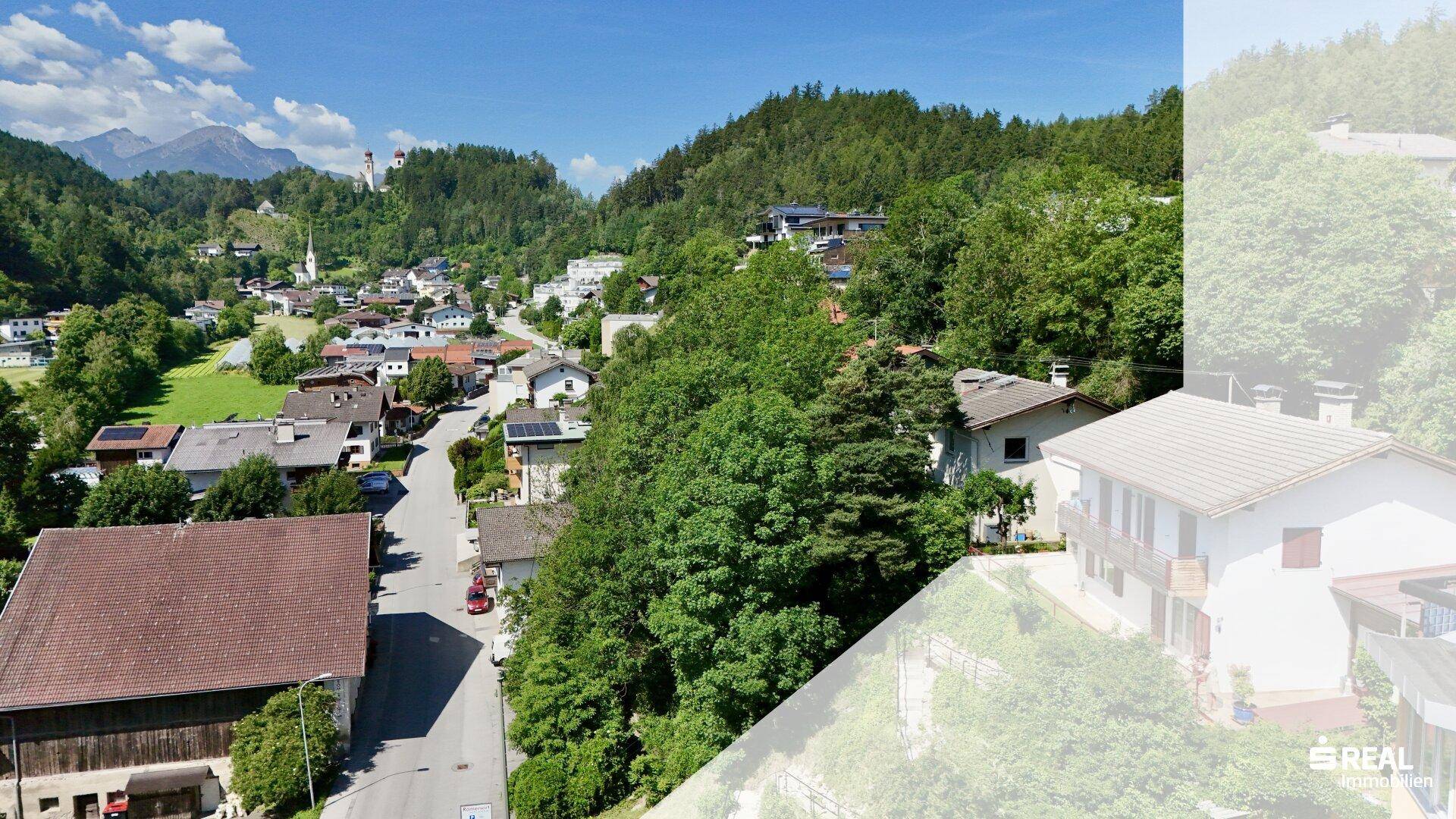 Panoramablick auf eine malerische Stadt im Tal, umgeben von grünen Hügeln und Bergen.