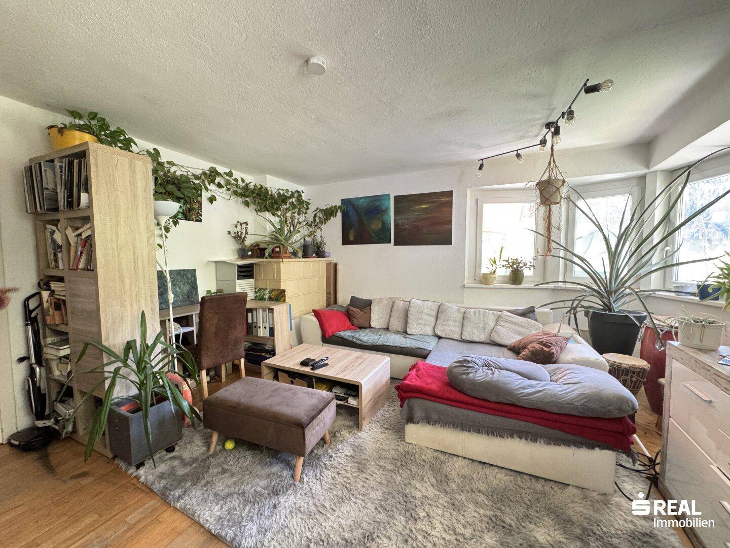 Helles Wohnzimmer mit großem Sofa, vielen Pflanzen und einem Bücherregal, das zum Entspannen einlädt.