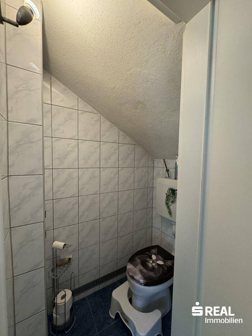 Weiterer Blick ins WC mit Dachschräge und gefliesten Wänden, funktional eingerichtet.