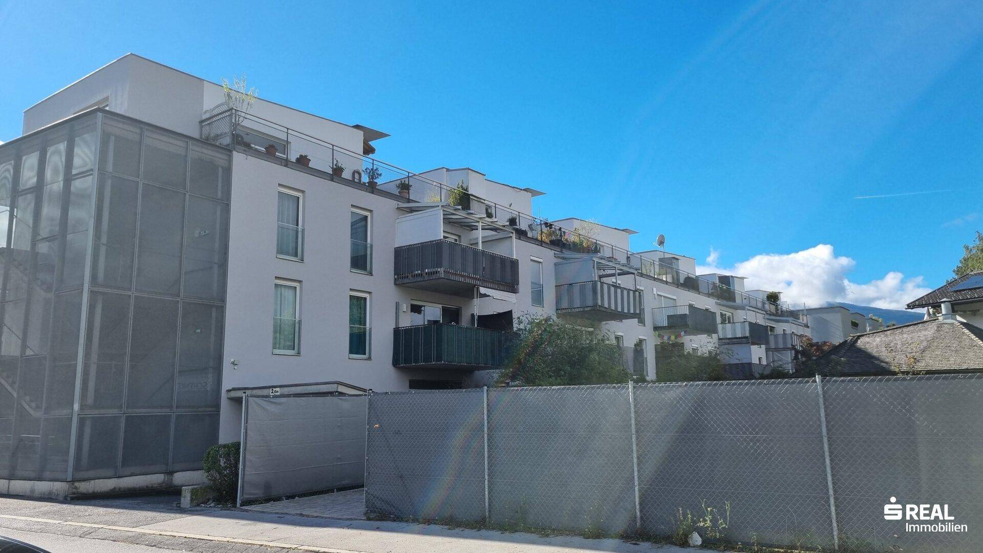 Seitenansicht eines modernen Wohngebäudes mit Balkonen und einer Gitterfassade unter blauem Himmel.