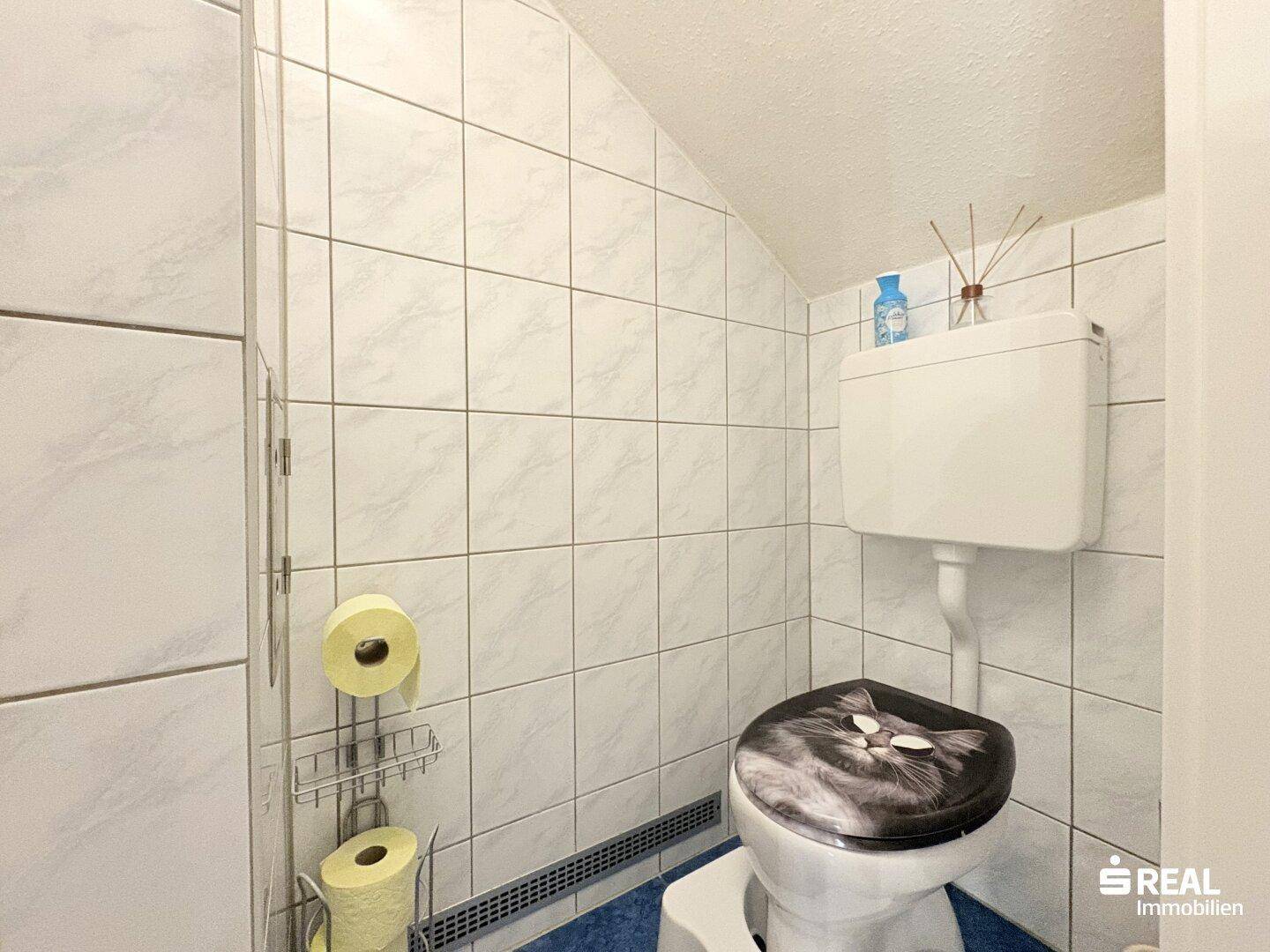 WC mit gefliesten Wänden und einer Dachschräge, einfach und sauber gehalten.