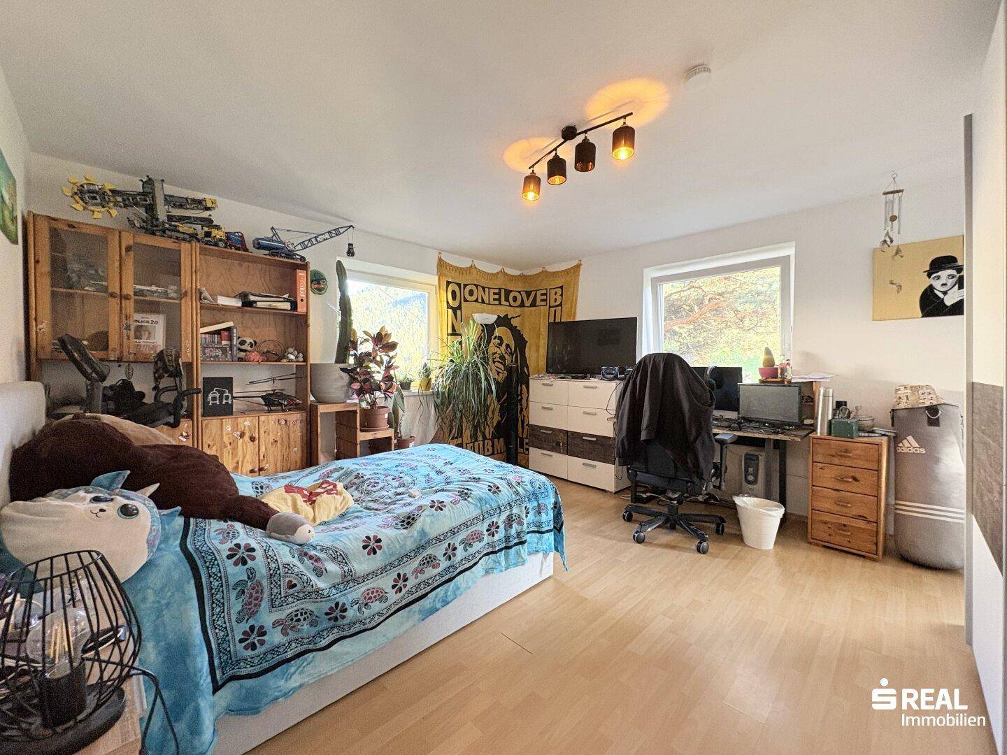 Helles Schlafzimmer mit Bett, Schreibtisch und Regalen, bietet einen Blick ins Grüne.