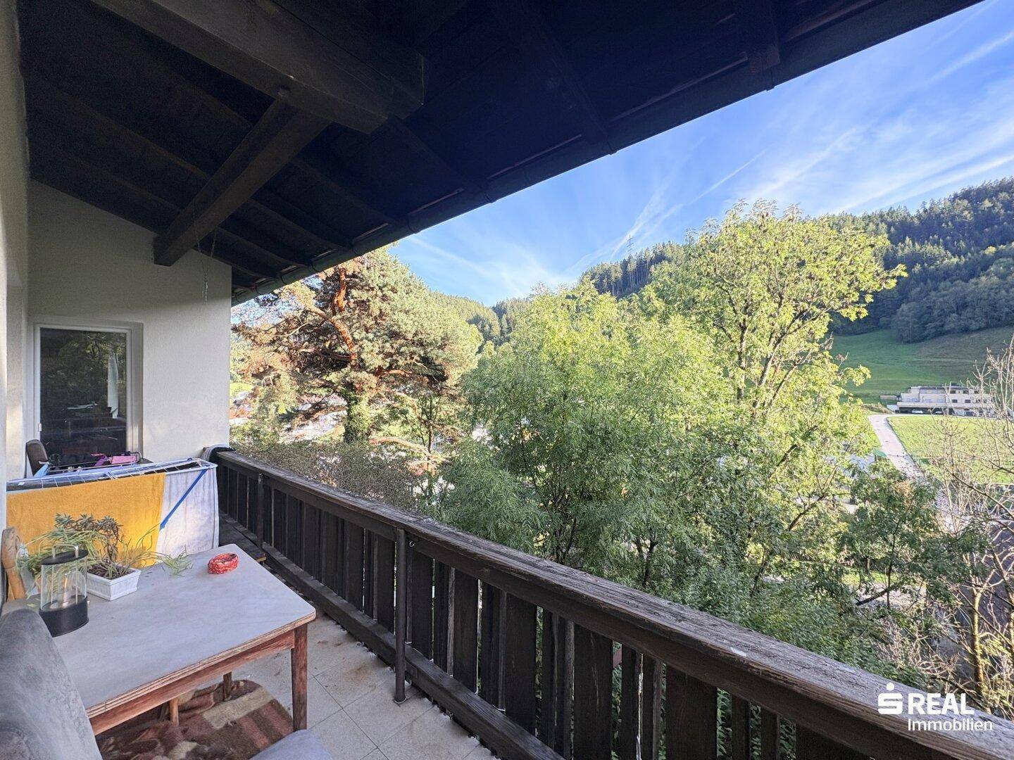 Gemütlicher Balkon mit Holzbalken und Blick ins Grüne, ausgestattet mit einem kleinen Tisch.