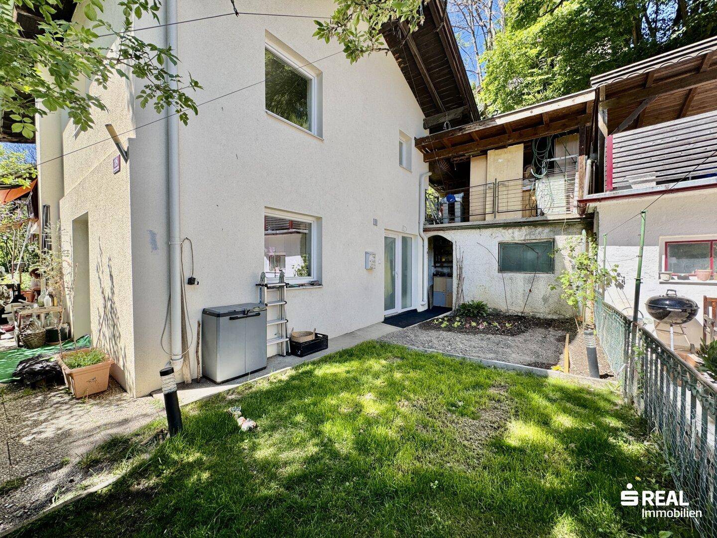 Hinterhof des Hauses mit einer kleinen Rasenfläche und einem gepflasterten Bereich.
