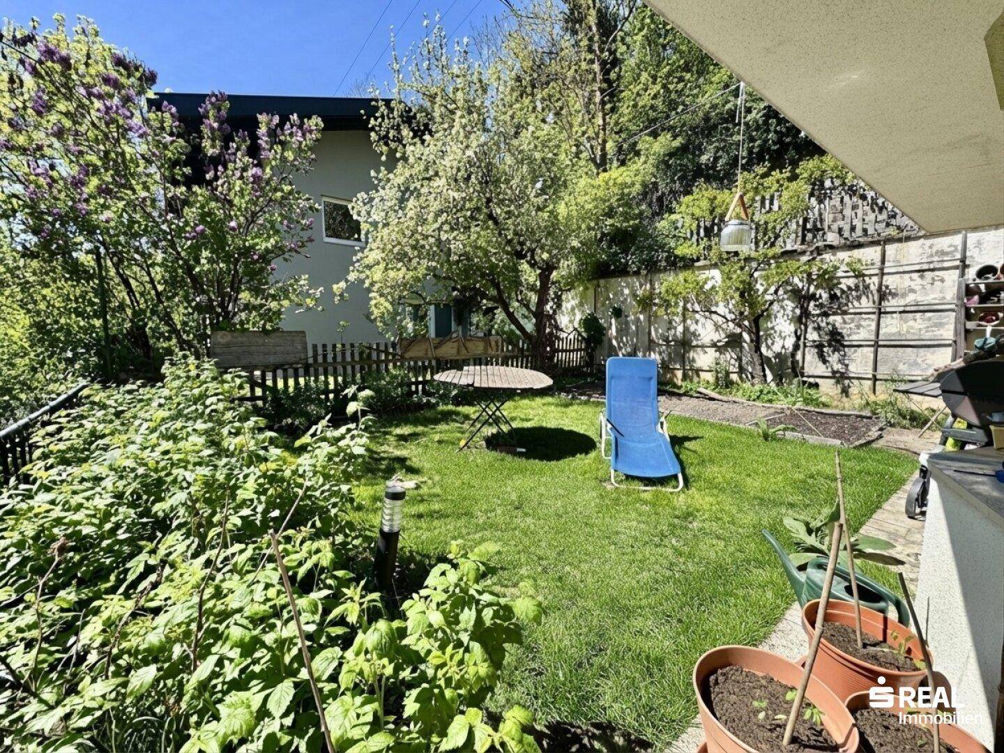 Kleiner, gepflegter Gartenbereich mit Rasen, Sitzgelegenheiten und blühenden Sträuchern.
