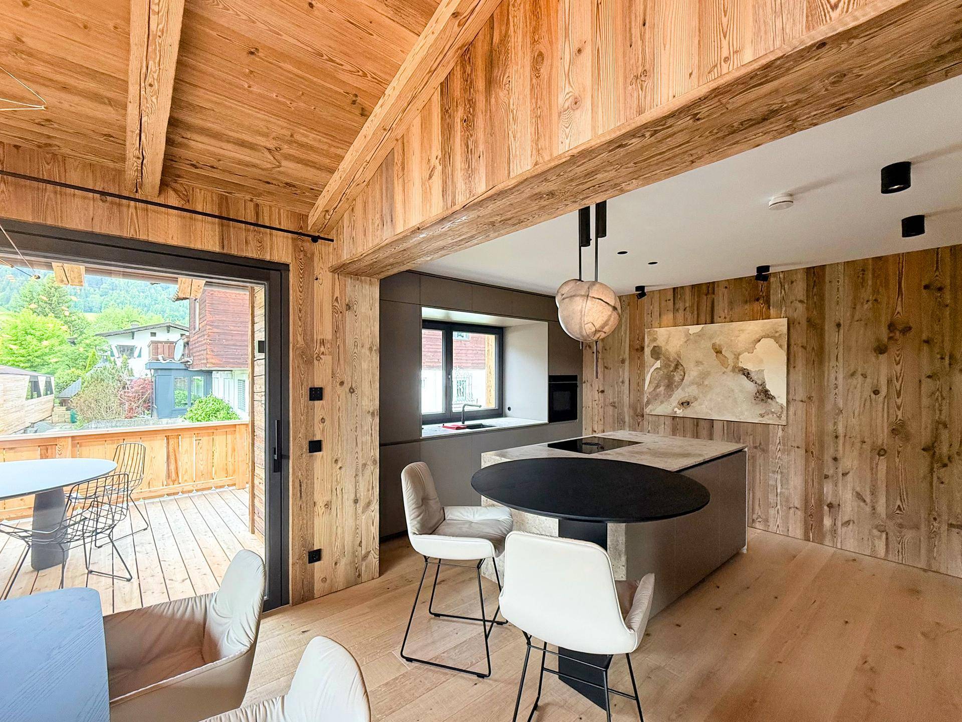 Moderne Küche mit Kochinsel, Essbereich und direktem Zugang zu einer Holzterrasse.