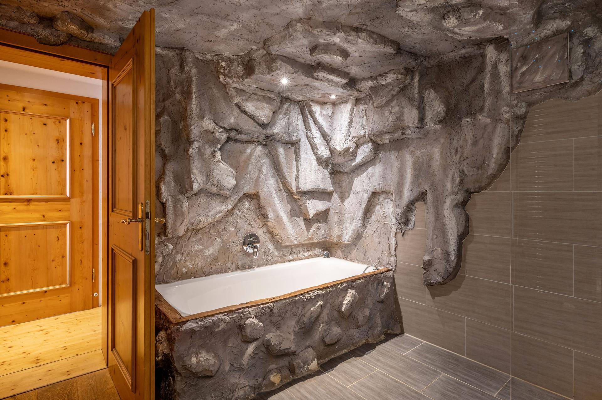 Badezimmer mit einer in Felsoptik integrierten Badewanne und rustikalen Holztüren.