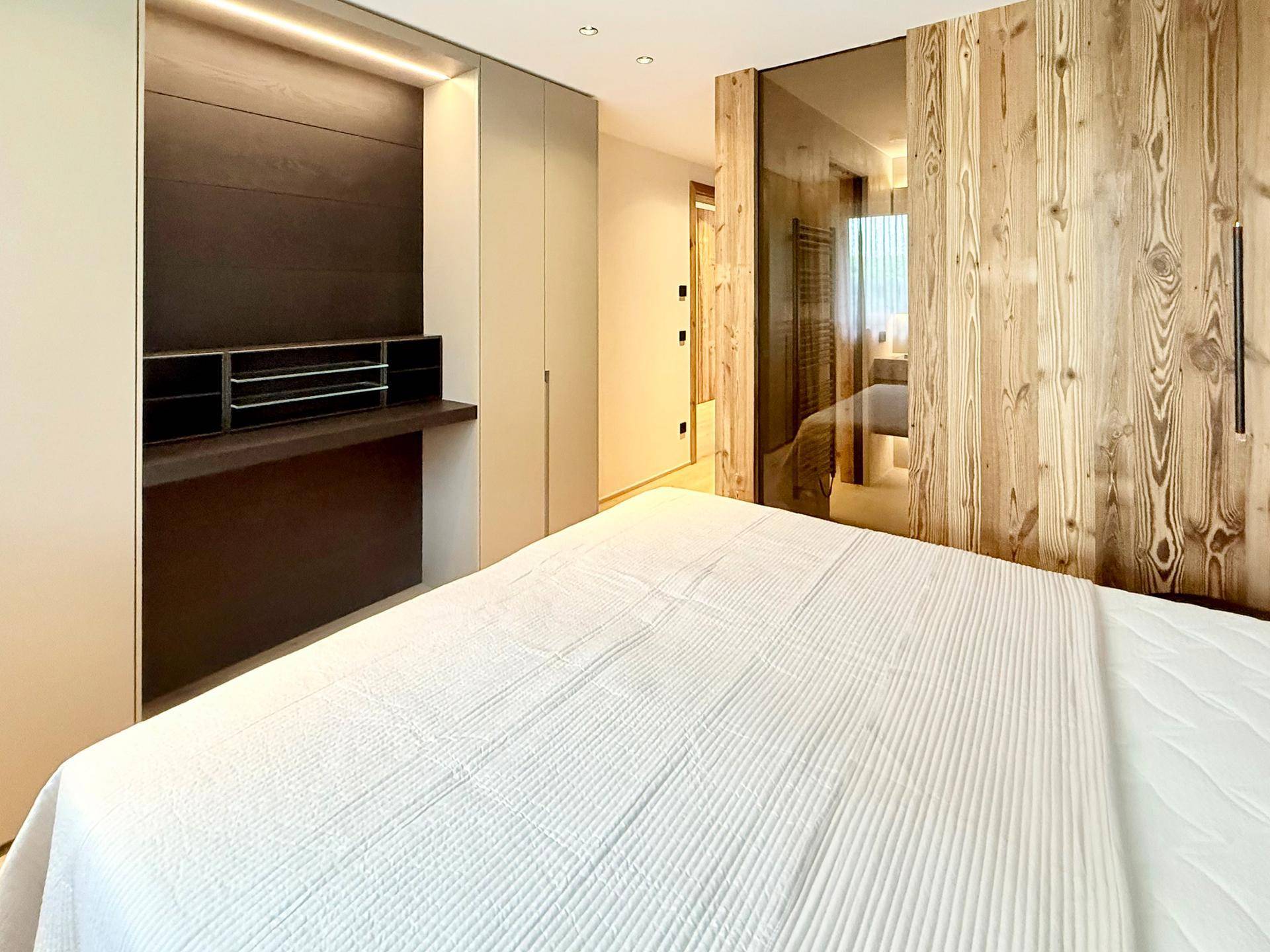 Schlafzimmer mit Holzwand, Spiegelschränken und integriertem Schreibtischbereich.