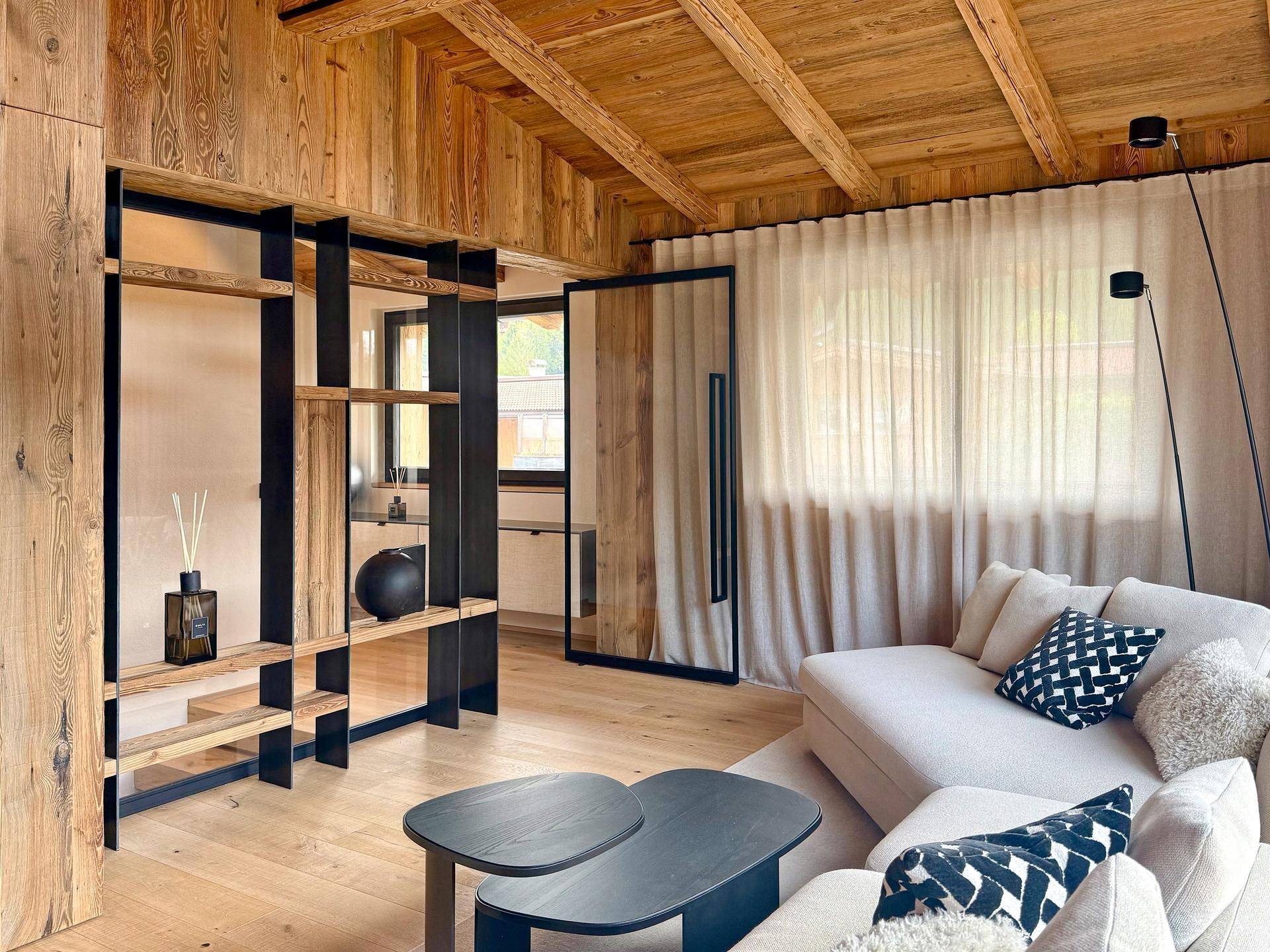 Gemütlicher Wohnbereich mit Holzwänden, Holzbalkendecke und modernen Möbeln.