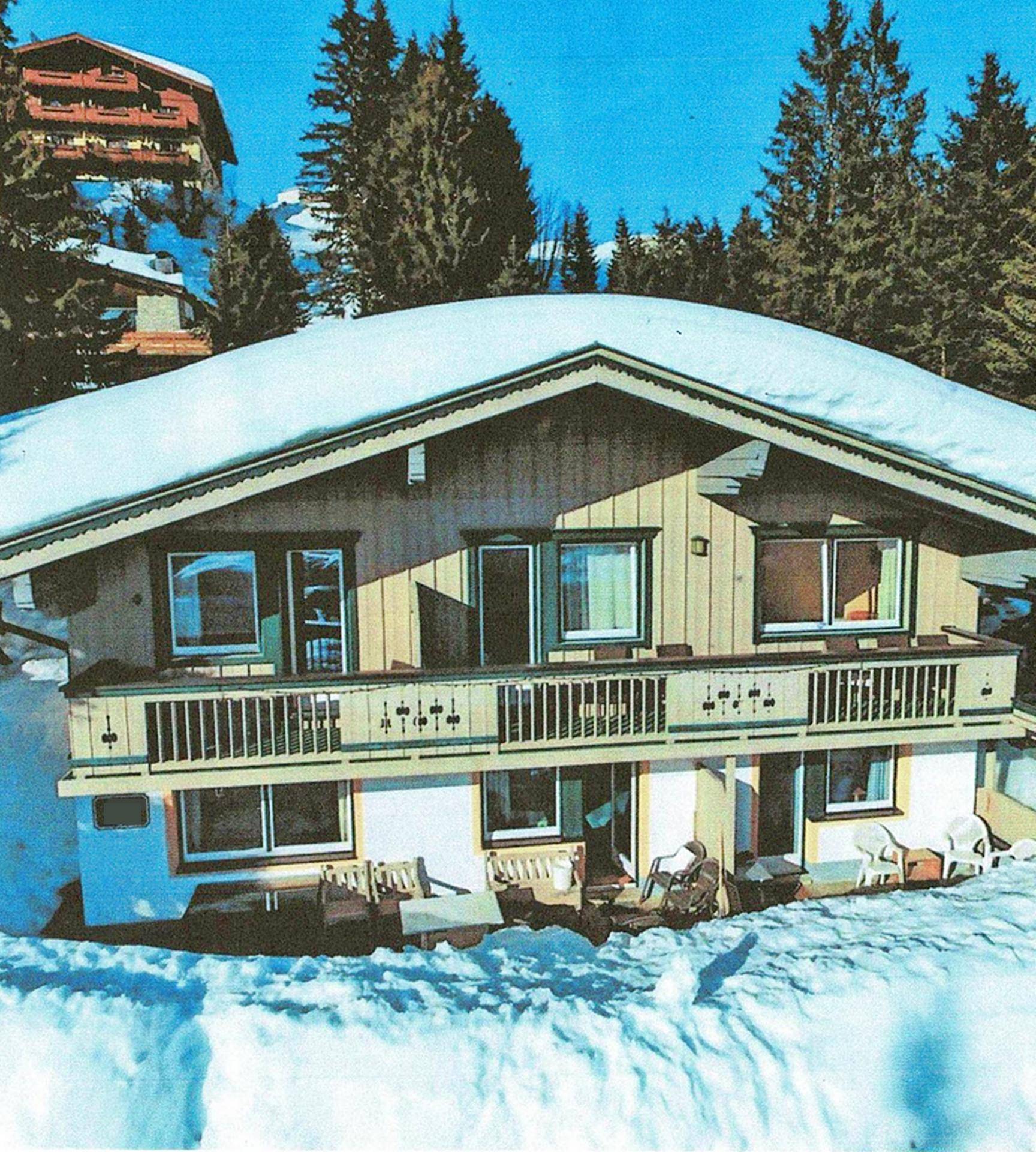 Traditionelles Chalet im Winter, bedeckt mit Schnee und umgeben von Nadelbäumen.