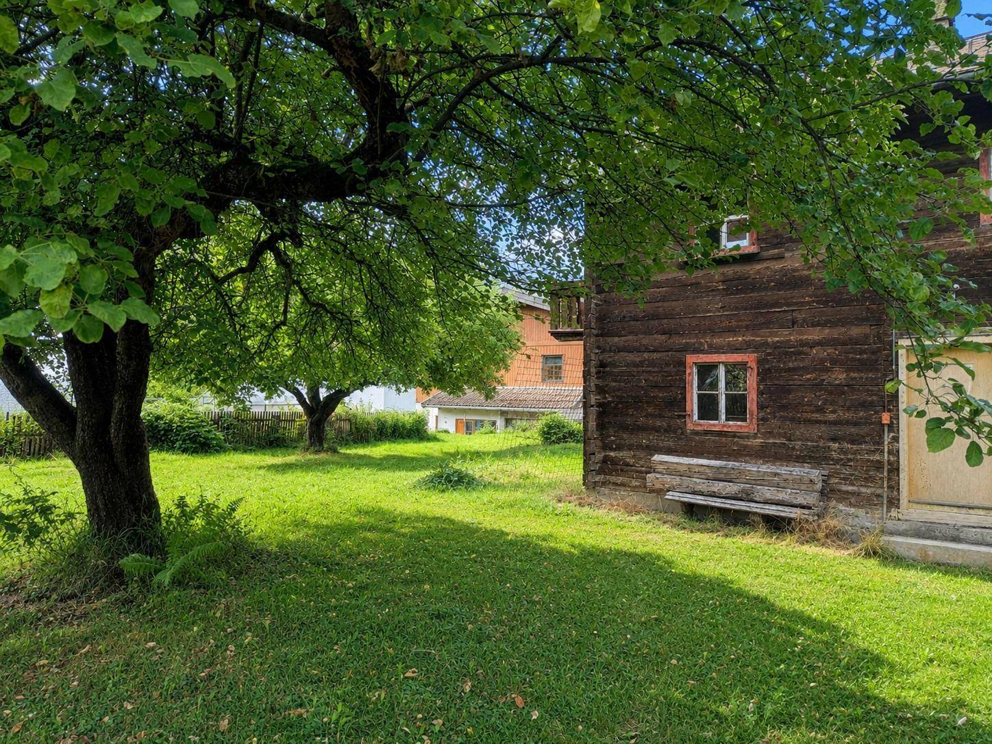 Idyllischer Gartenbereich mit altem Baumbestand und dem traditionellen Holzhaus im Hintergrund.