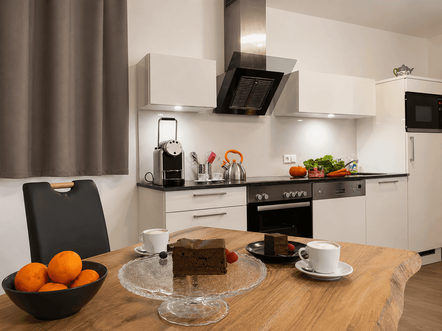 Helle Küche mit moderner Ausstattung, Holztisch und Kuchenstücken für eine gemütliche Kaffeepause.
