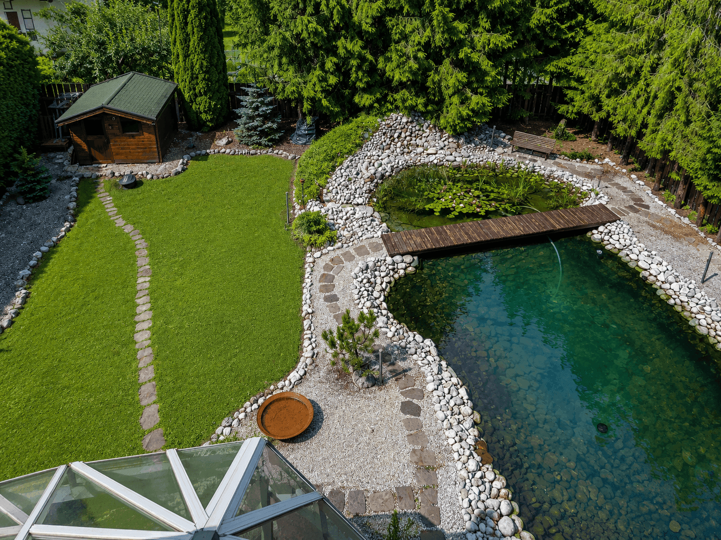 Weitläufiger Gartenbereich mit Naturteich, Holzsteg, Gartenhaus und gepflegtem Rasen.