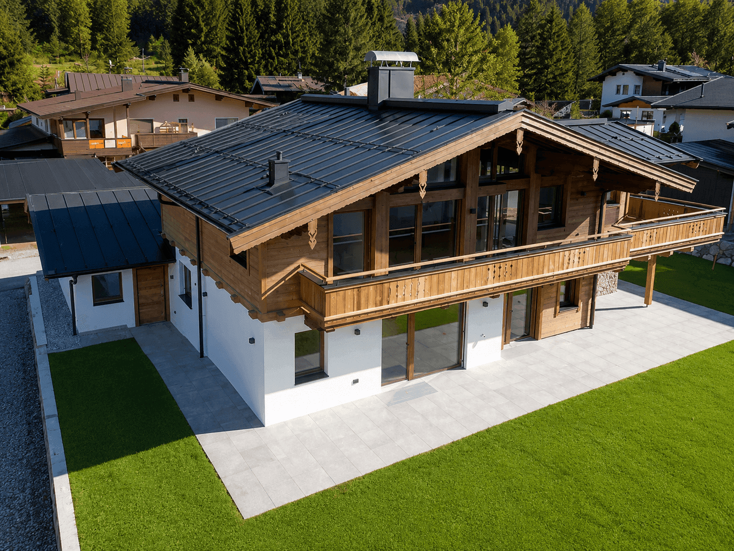 Luftaufnahme des Holzchalets mit schwarzem Dach, umgeben von Natur und anderen Häusern.