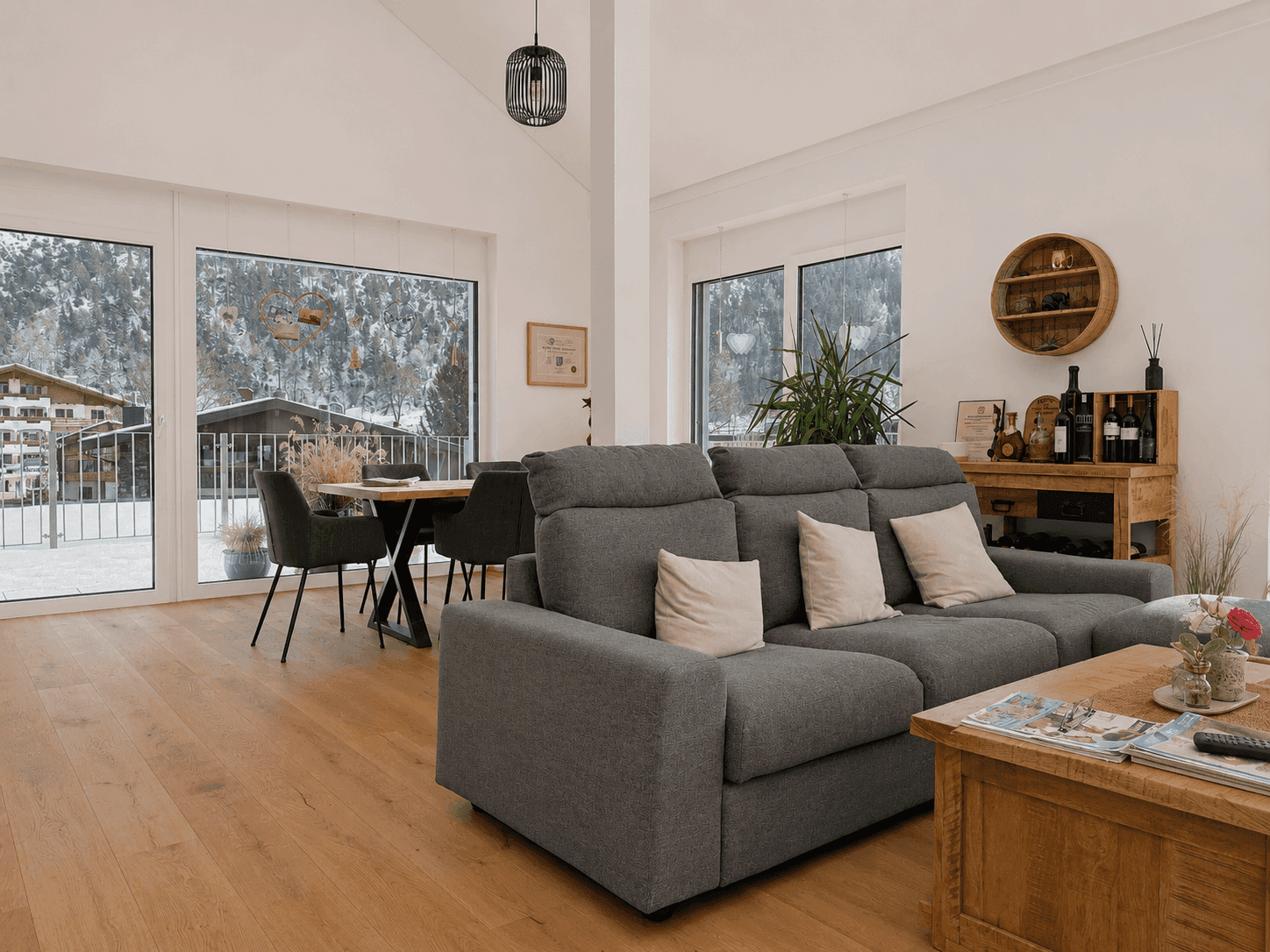 Offener Wohn- und Essbereich mit bequemer Couch, Holzboden und Panoramablick auf die Berge.