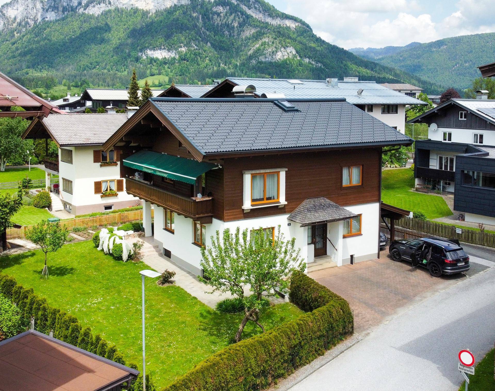 Luftaufnahme eines gepflegten Einfamilienhauses in alpiner Umgebung mit Bergblick und Garten.