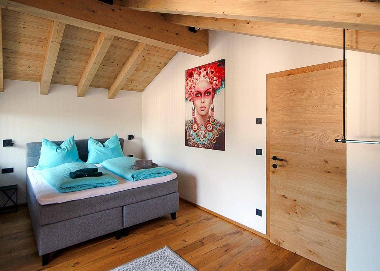 Modernes Schlafzimmer mit Holzbalkendecke, Holzboden und farbenfrohem Kunstwerk.