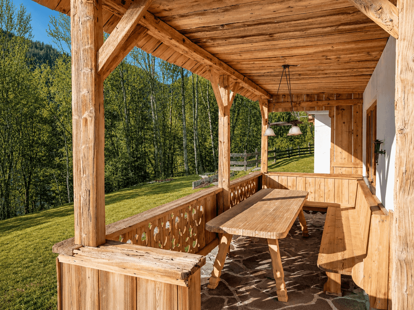 Überdachte Holzterrasse mit rustikalen Möbeln und Blick auf die umliegende grüne Landschaft.