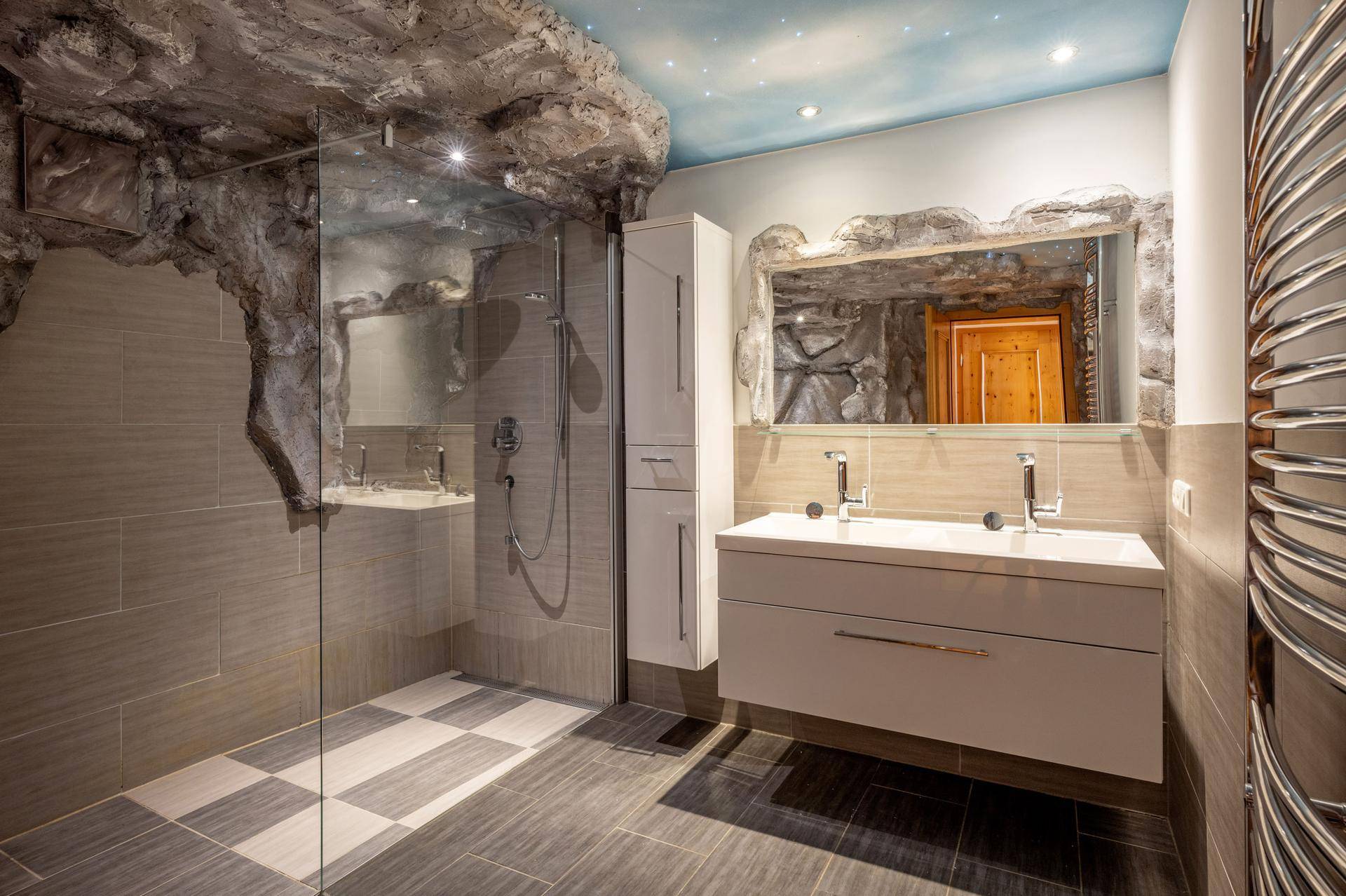 Modernes Badezimmer mit begehbarer Dusche, Doppelwaschbecken und einzigartiger Felswandgestaltung.