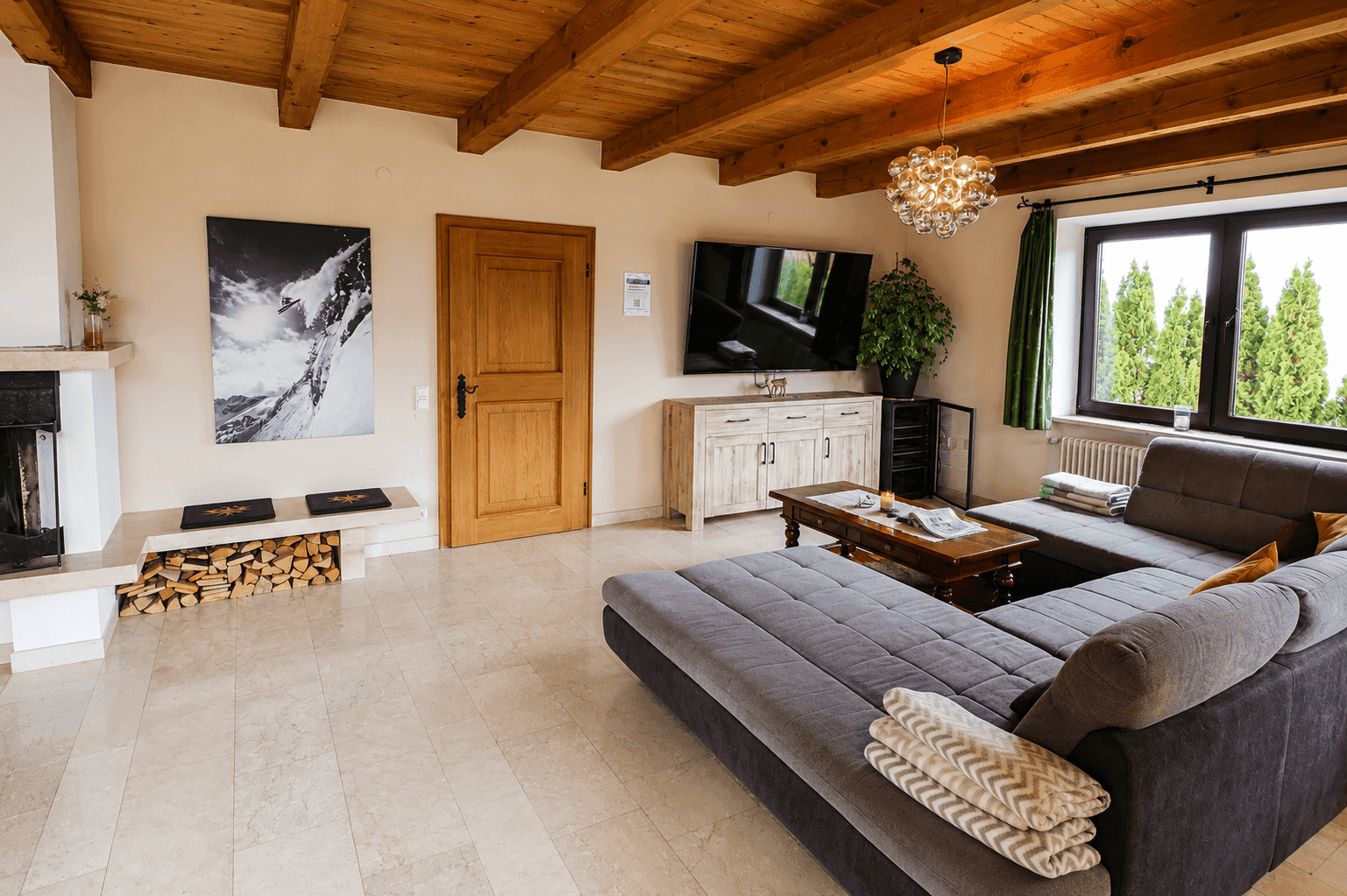 Heller Wohnbereich mit großem Sofa, Kamin und Blick auf die umliegende Natur.