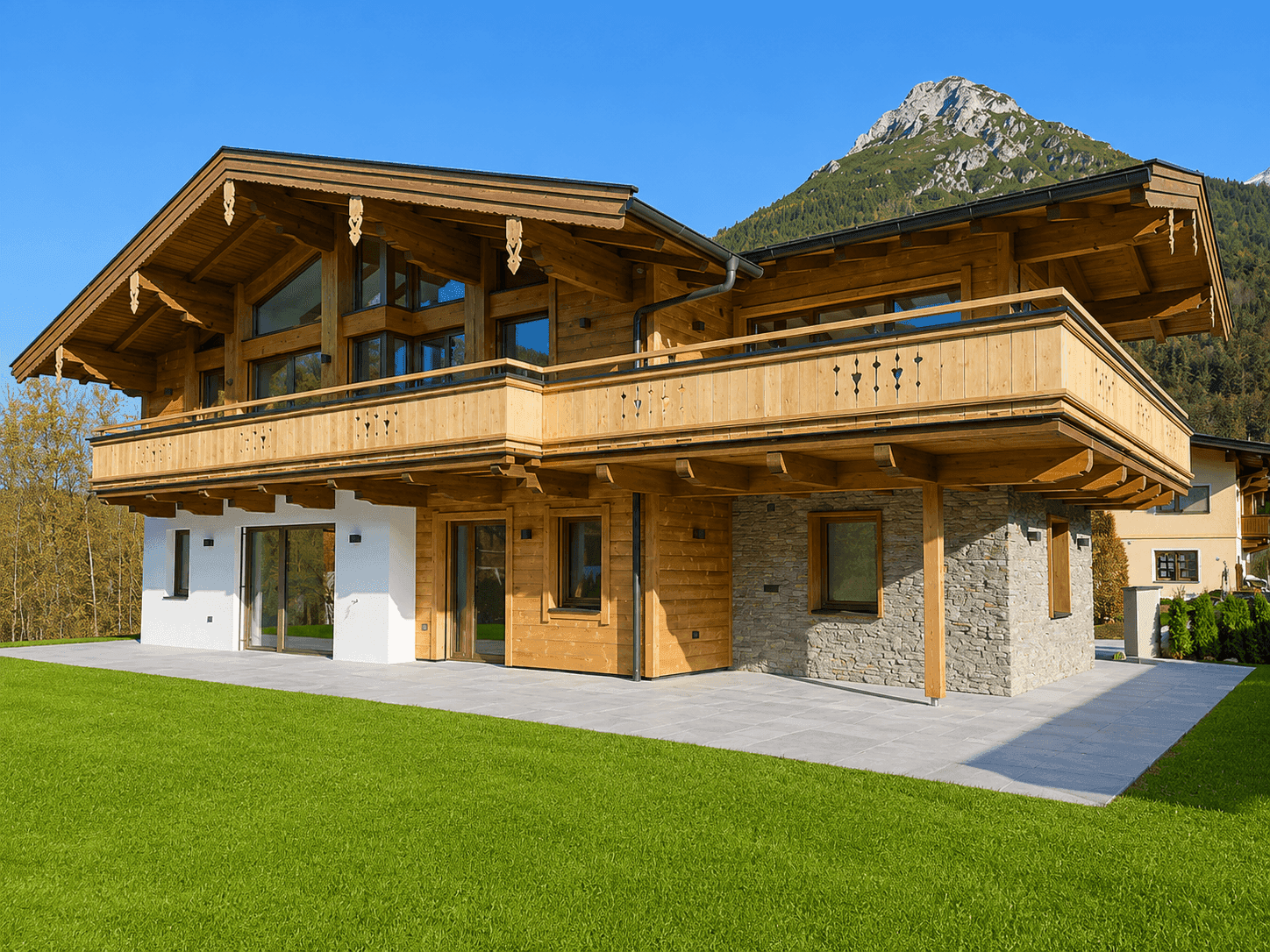 Modernes Holzchalet mit Steinelementen, weitläufigem Rasen und beeindruckendem Bergpanorama.